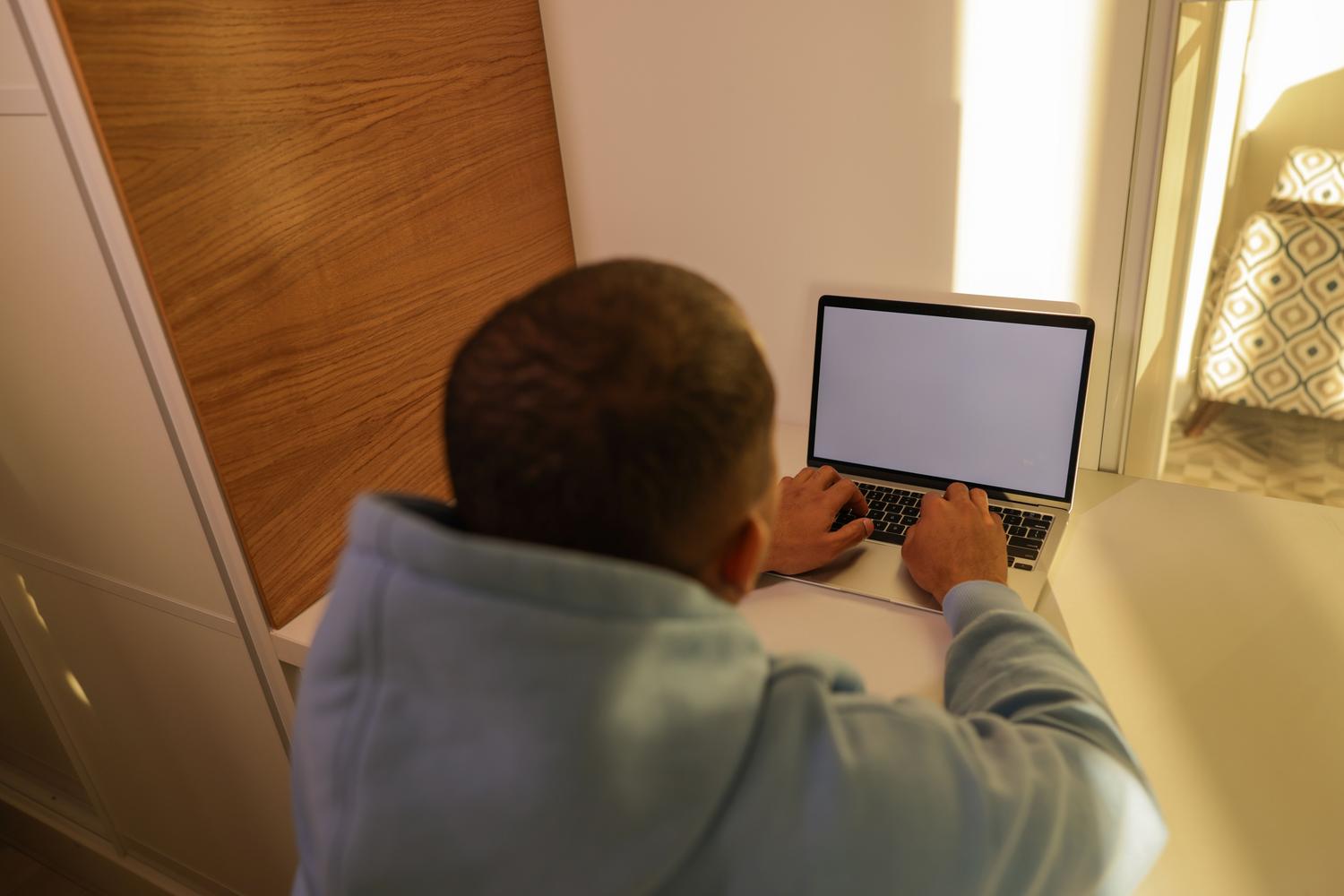 Hombre joven utilizando un ordenador portátil en un escritorio minimalista con iluminación natural cálida.