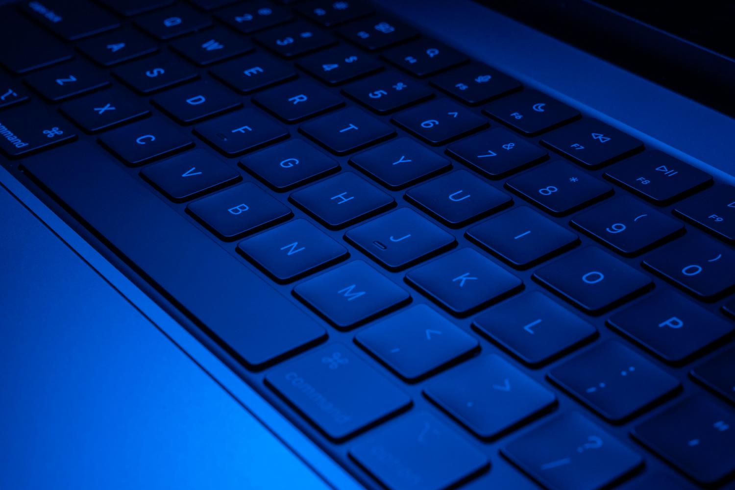 Teclado de laptop retroiluminado en azul eléctrico, evocando una atmósfera de herramienta secreta, avanzada y tecnológica.