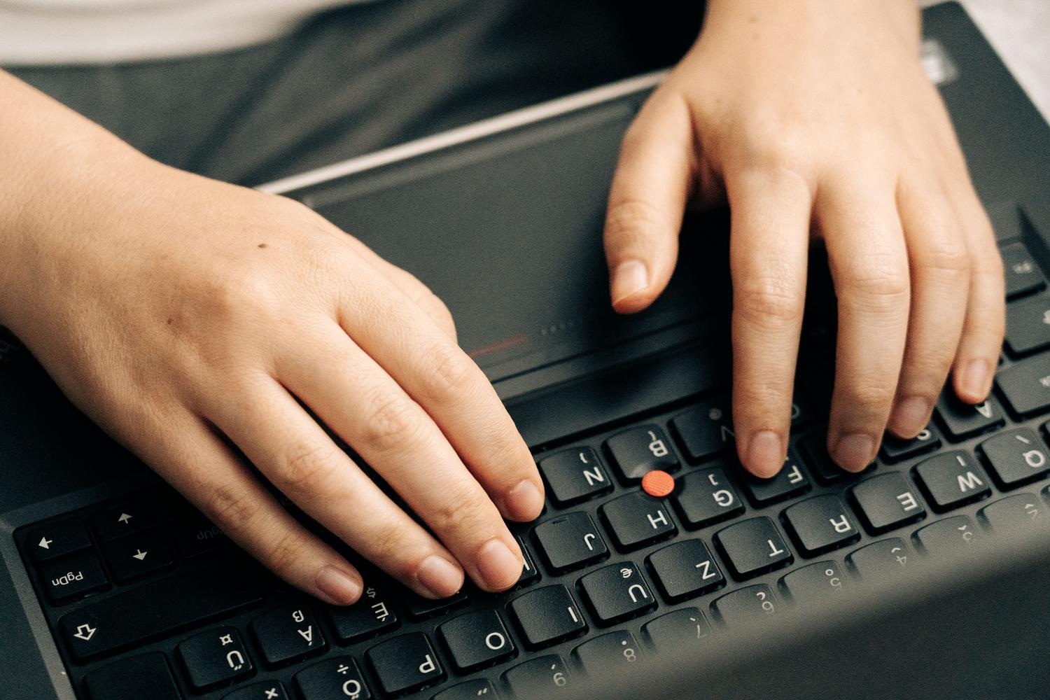 Manos de un usuario escribiendo en un teclado de laptop profesional, transmitiendo la acción de configurar el sistema y la productividad.