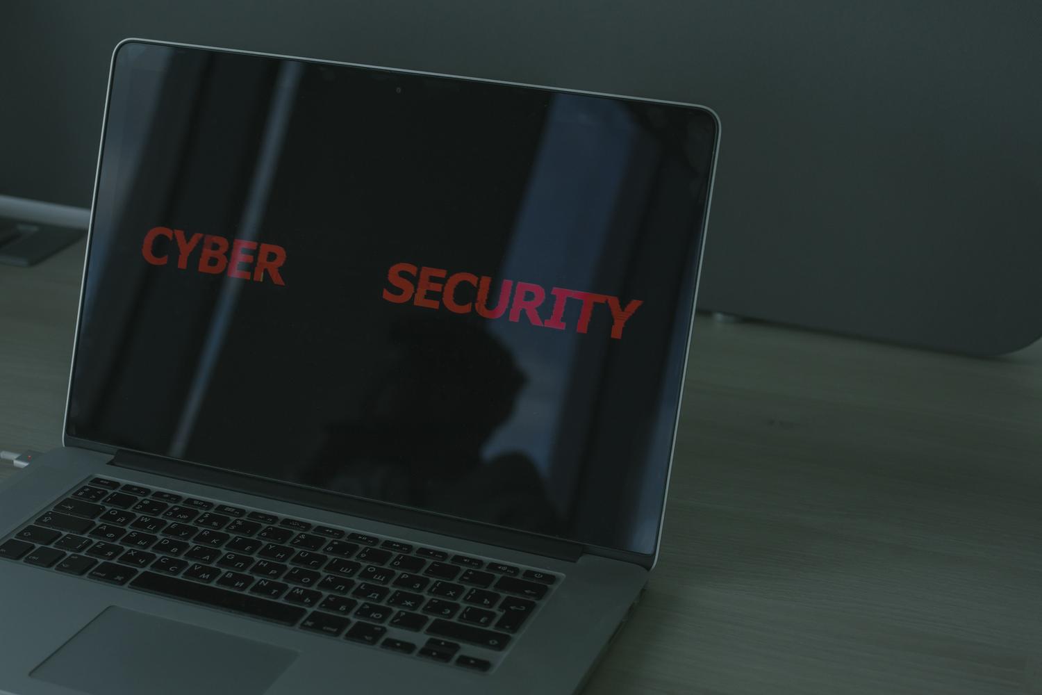 Laptop sobre un escritorio con la pantalla mostrando el texto 'CYBER SECURITY' en rojo, enfatizando la protección de datos.