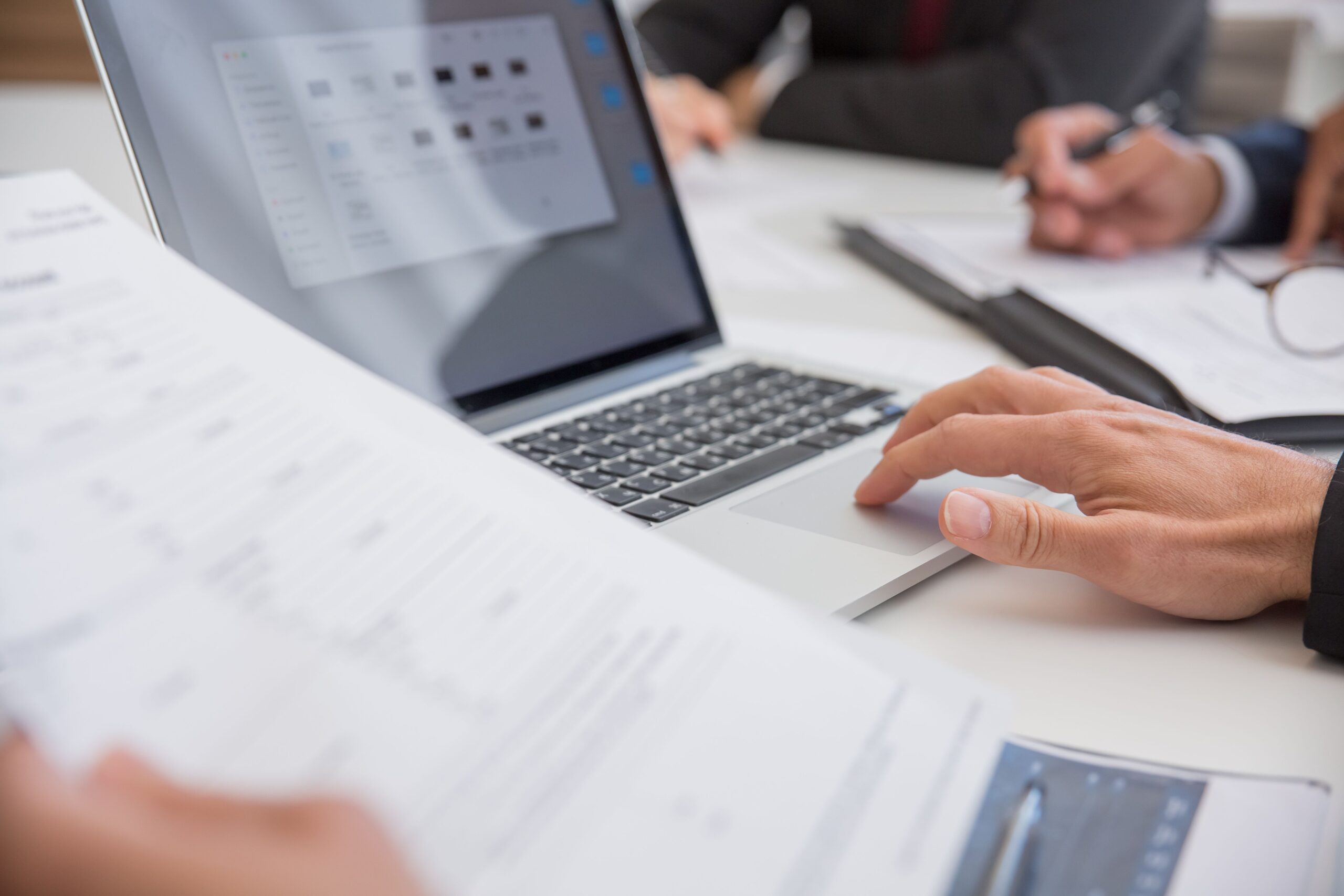 Primer plano de manos trabajando con documentos digitales en un ordenador portátil en un entorno profesional.