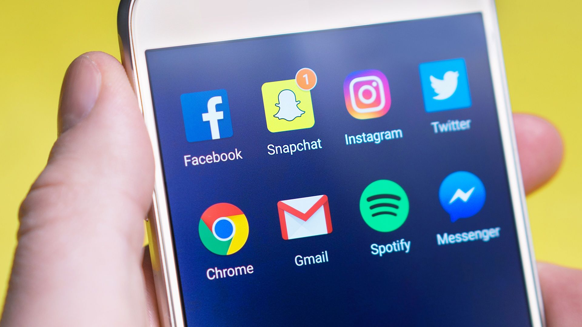 Primer plano de una mano sosteniendo un smartphone con iconos de aplicaciones de redes sociales sobre un fondo amarillo vibrante. Primer plano de una mano sosteniendo un smartphone con iconos de aplicaciones de redes sociales sobre un fondo amarillo vibrante.