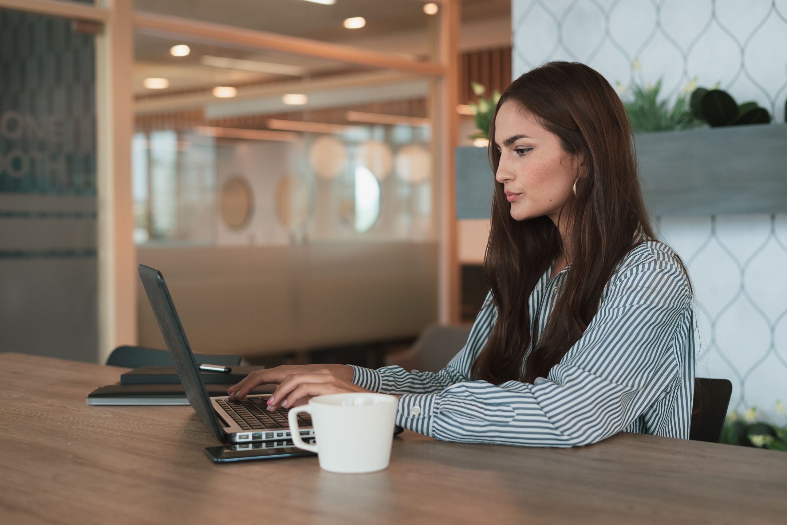 Mujer profesional trabajando con un ordenador portátil en una oficina moderna y luminosa, ilustrando la productividad y gestión diaria.