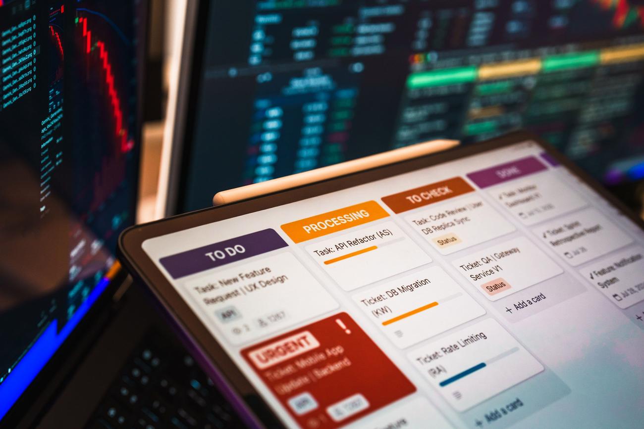 Tablero Kanban digital en una tablet con dashboards de análisis de datos al fondo, ilustrando la fase de planificación del SDLC.