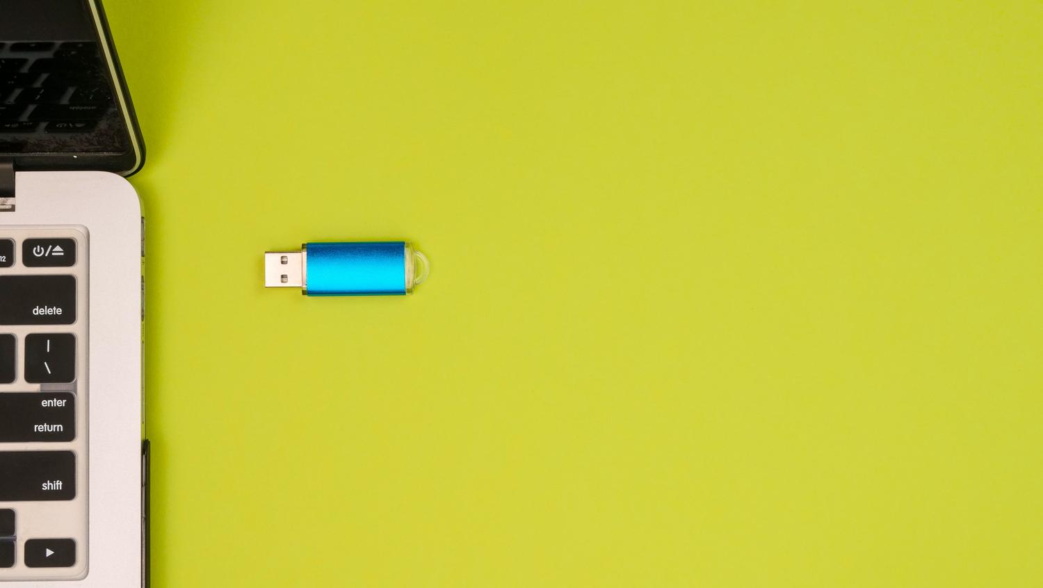 Memoria USB junto a un portátil, representando la configuración necesaria para gestionar múltiples ISOs.