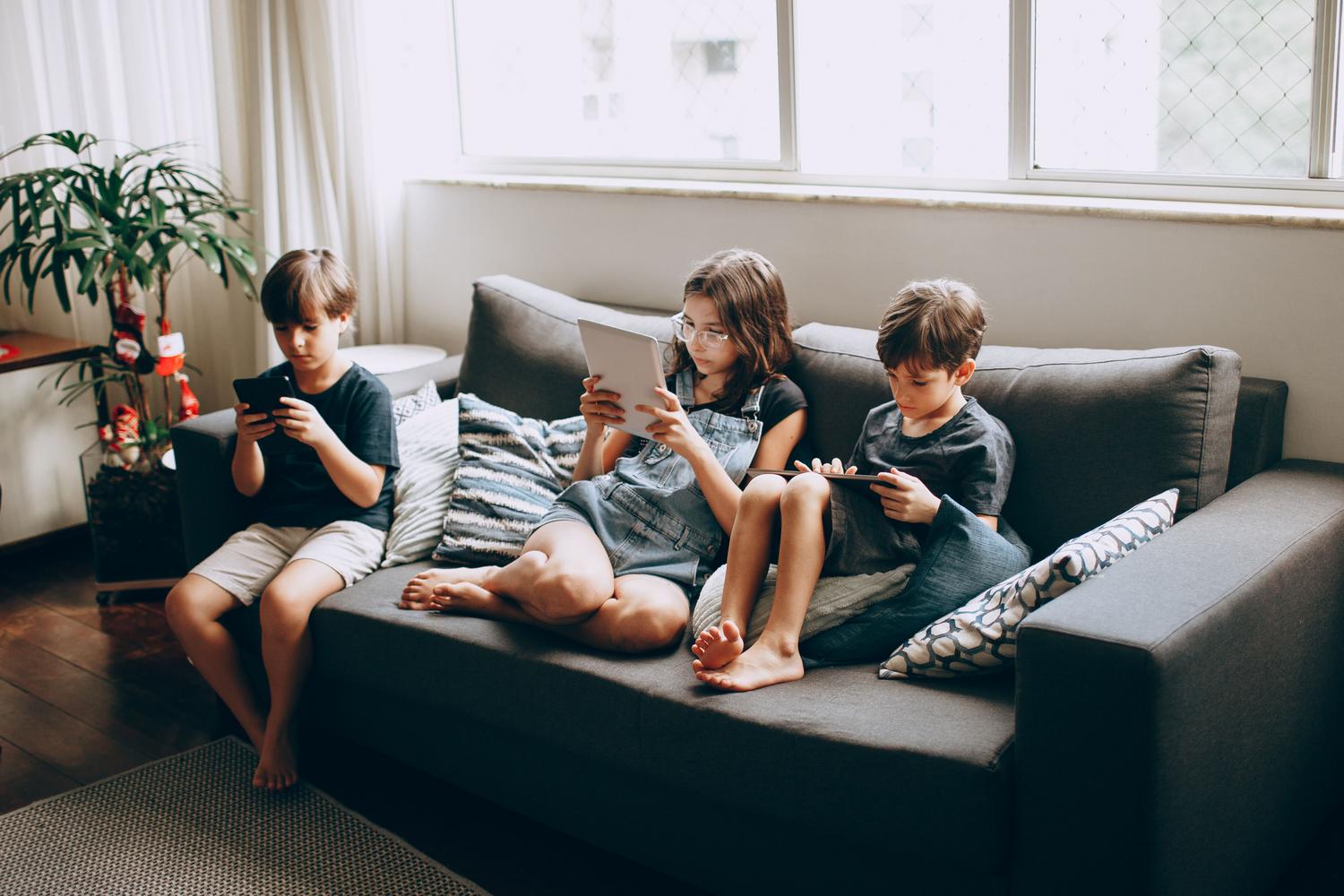 Tres niños sentados en un sofá utilizando tablets y smartphones conectados a la red doméstica