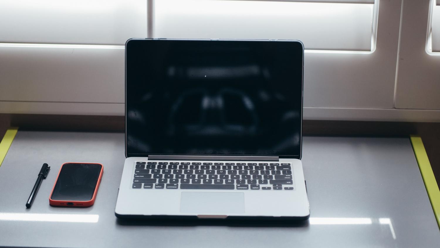 Setup minimalista de escritorio con portátil y smartphone bajo luz natural, ideal para un entorno de trabajo productivo y sin distracciones.