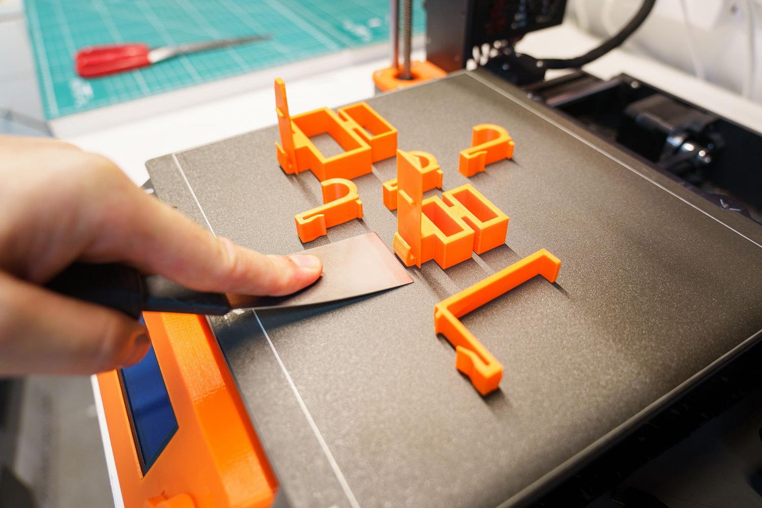Retirada de una pieza plástica naranja recién impresa de la cama de la impresora 3D Retirada de una pieza plástica naranja recién impresa de la cama de la impresora 3D