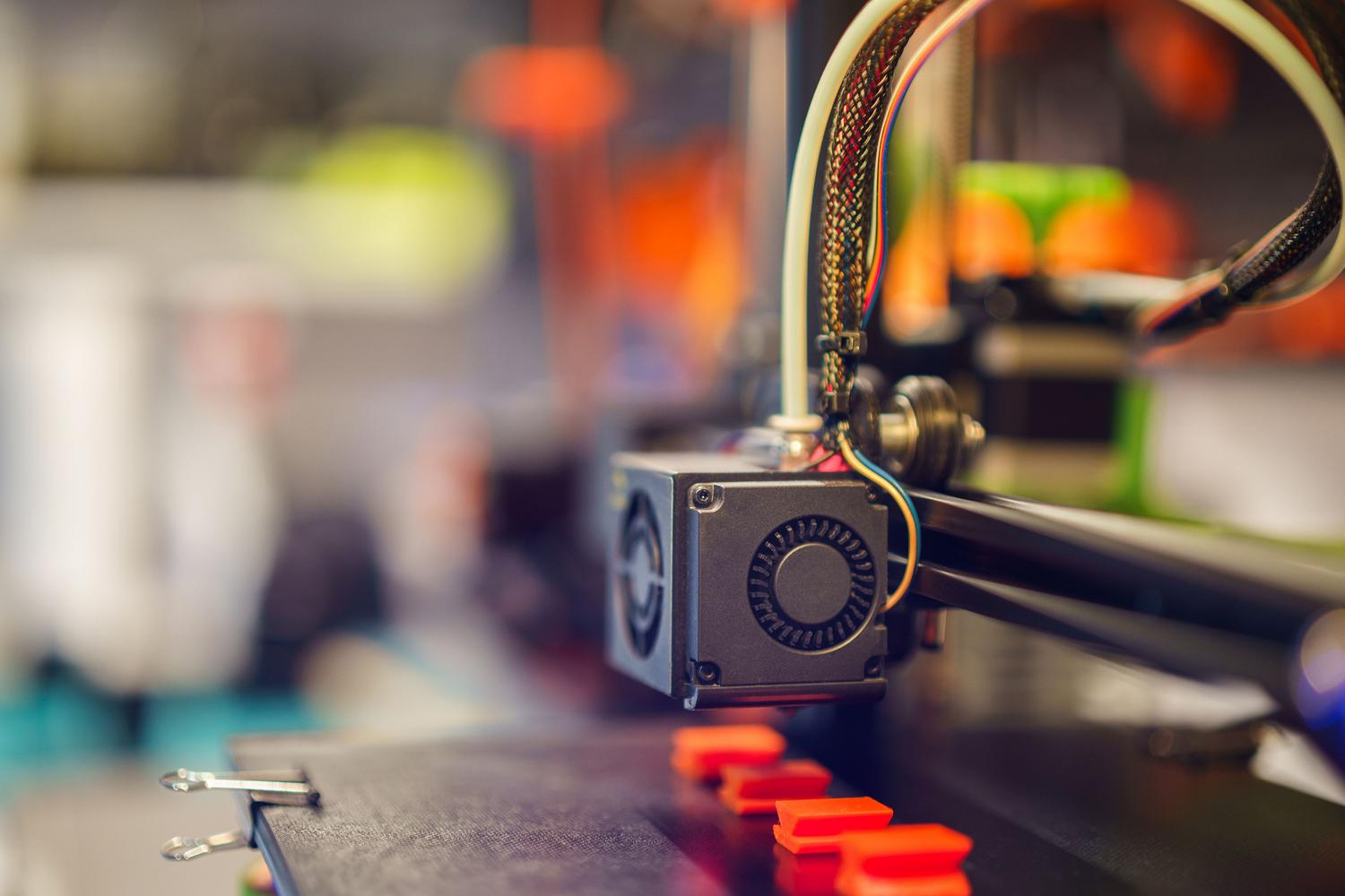 Primer plano de una boquilla de impresora 3D extruyendo filamento plástico rojo.