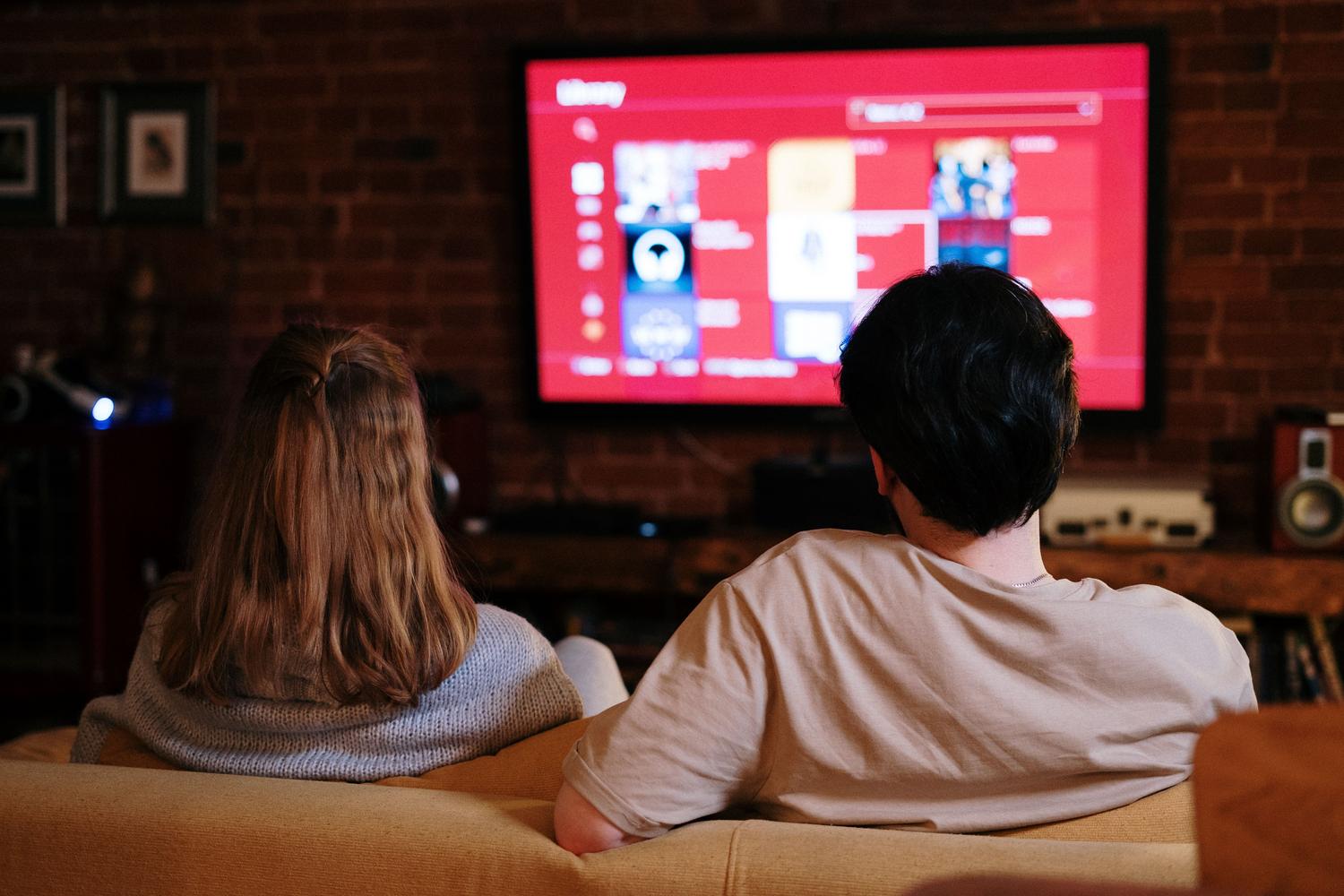 Pareja disfrutando de una biblioteca de películas en su televisor, ilustrando la experiencia de usuario de un servidor multimedia local.