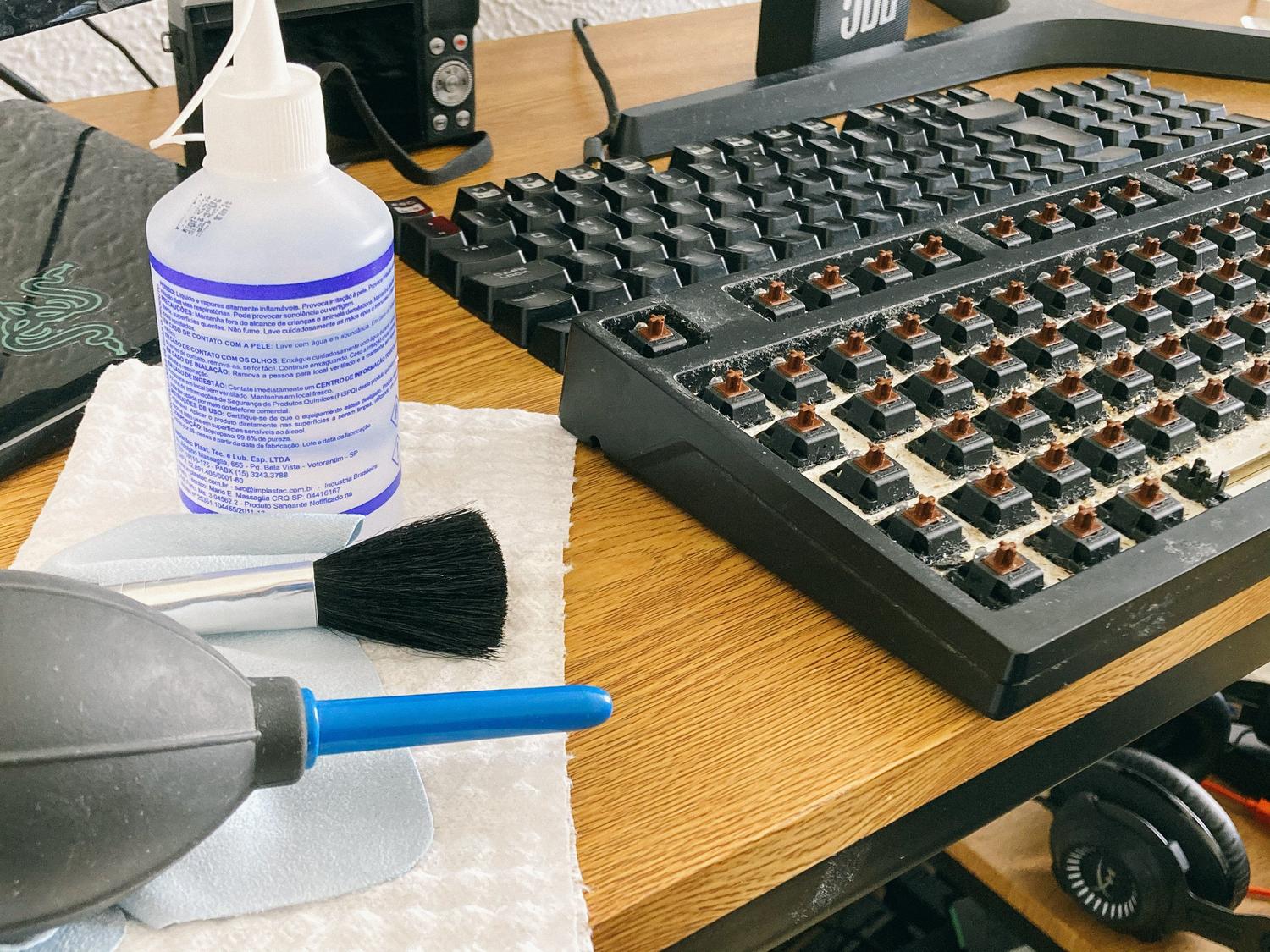 Kit de limpieza para teclado mecánico con alcohol isopropílico, pincel y soplador de aire sobre un escritorio.