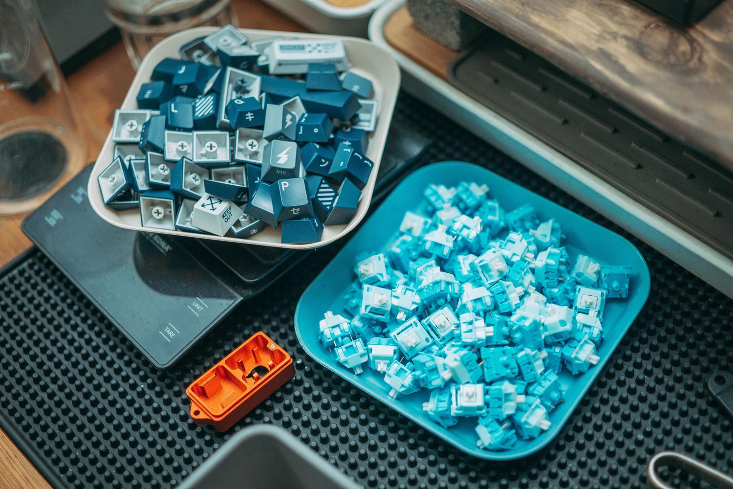 Set de herramientas para modding de teclados mecánicos con switches, teclas y un abridor de switches sobre una alfombrilla de trabajo.