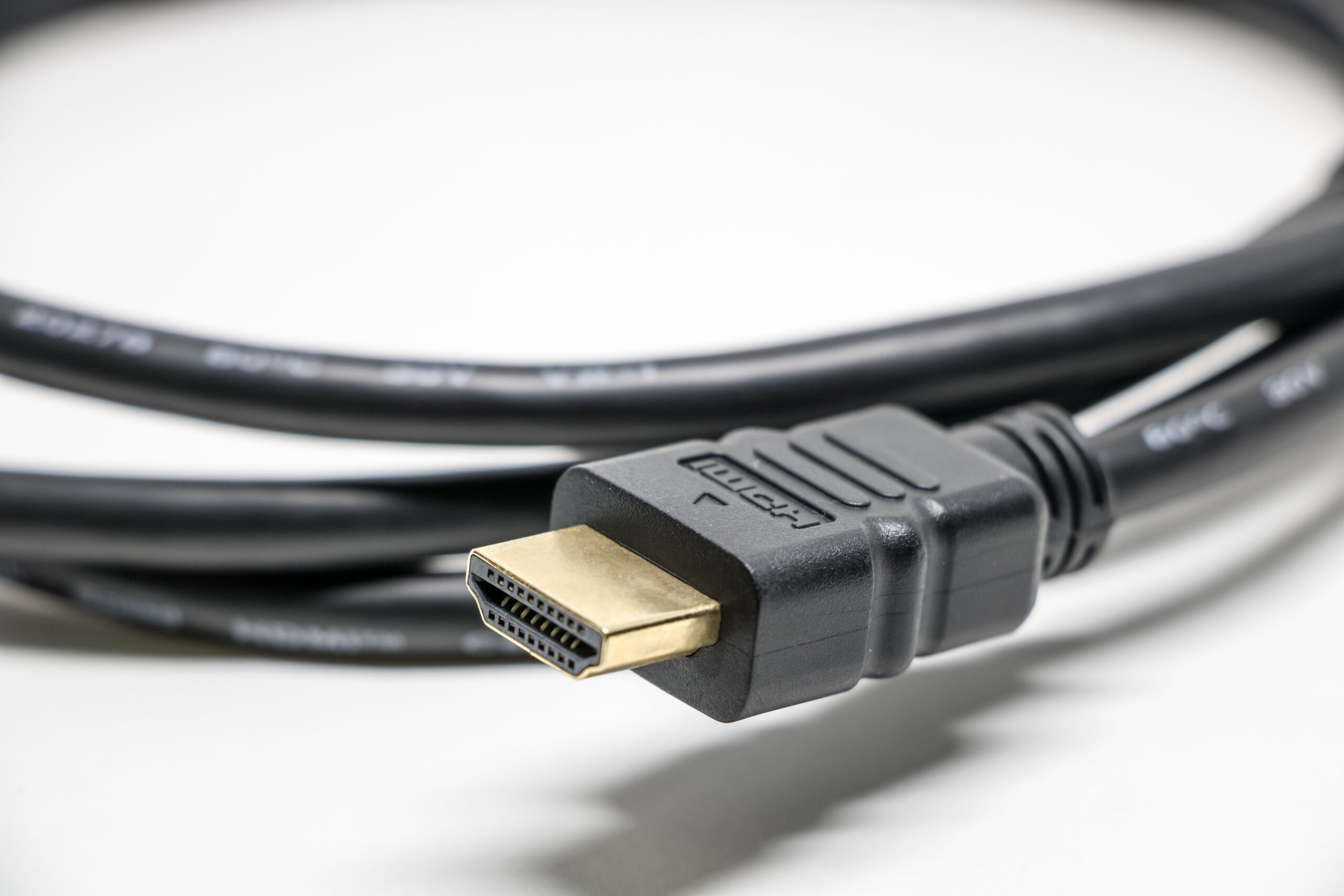 Primer plano detallado de un cable HDMI negro con conectores dorados sobre un fondo blanco.