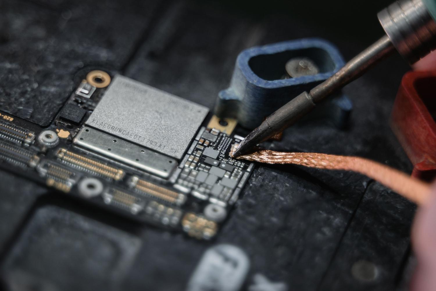 Detalle extremo de un soldador trabajando sobre una placa de circuito, representando la técnica de microsoldadura para reconstruir pistas de cobre.