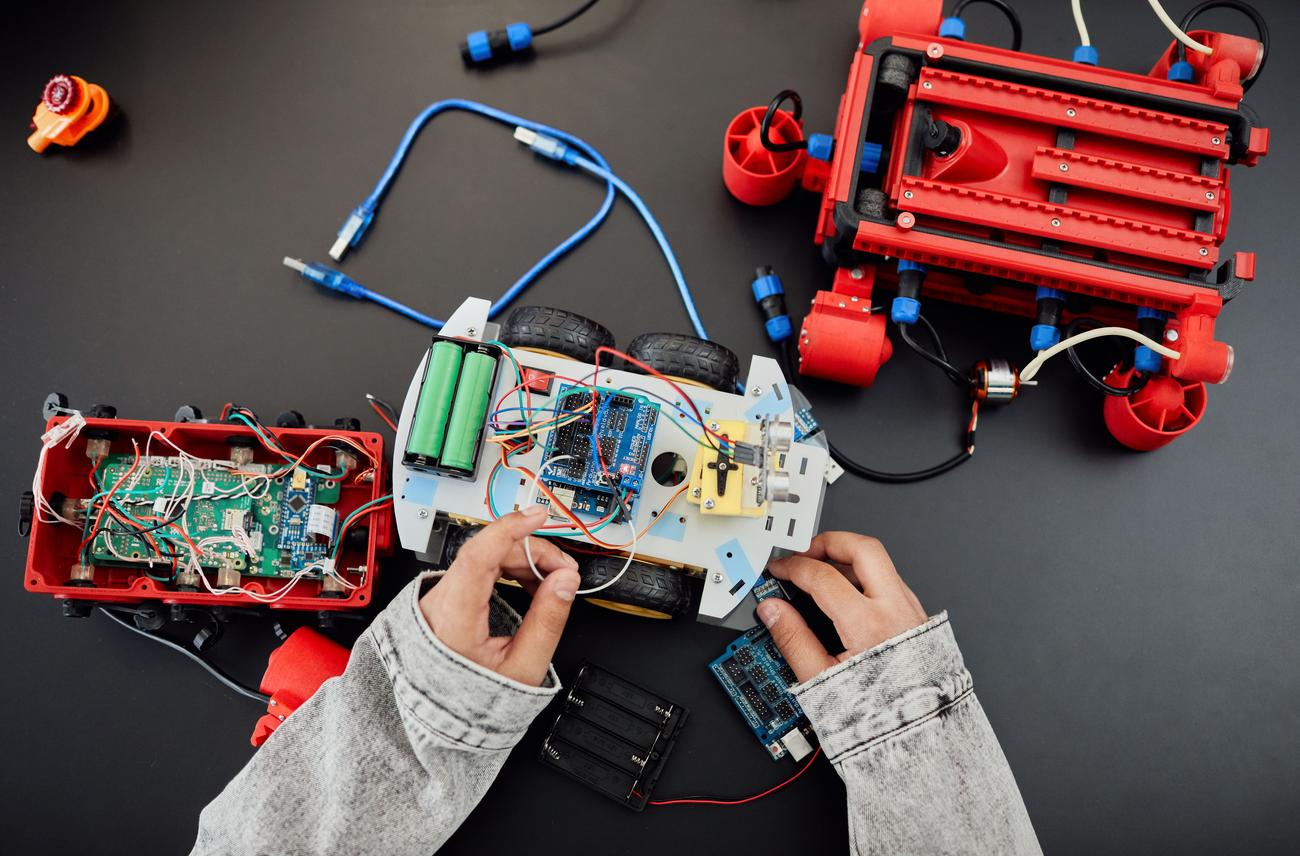 Manos jóvenes ensamblando un robot programable con circuitos electrónicos y ruedas