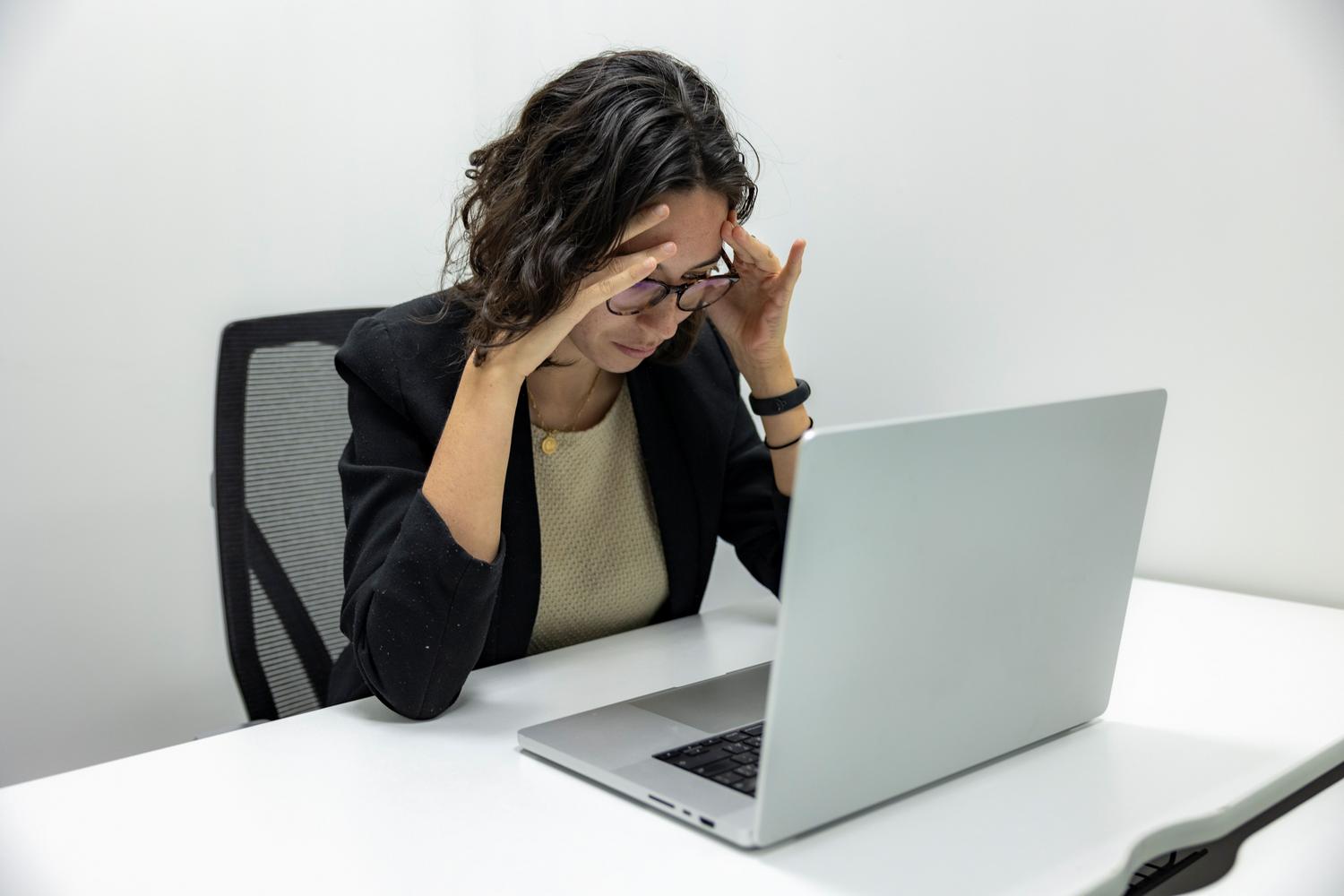 Mujer joven estresada trabajando con su ordenador en la oficina, reflejando la frustración por fallos técnicos en el software.