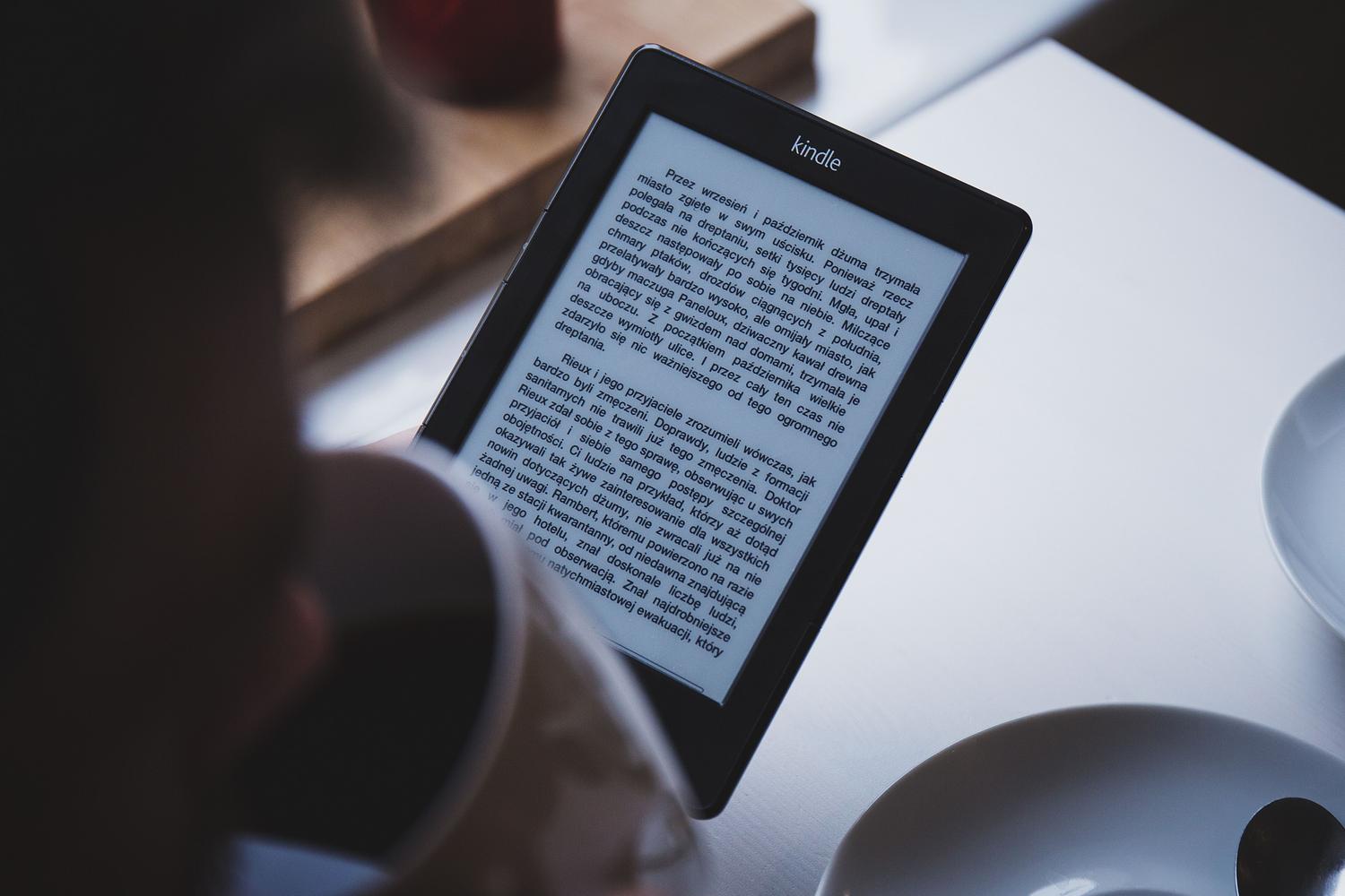Persona utilizando un lector de libros electrónicos mientras toma un café en un ambiente acogedor, mostrando el uso cotidiano de la tinta electrónica.