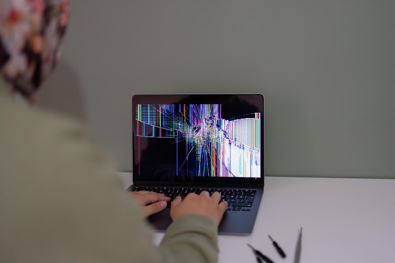 Una persona intentando trabajar en un portátil con la pantalla agrietada. Una persona intentando trabajar en un portátil con la pantalla agrietada.