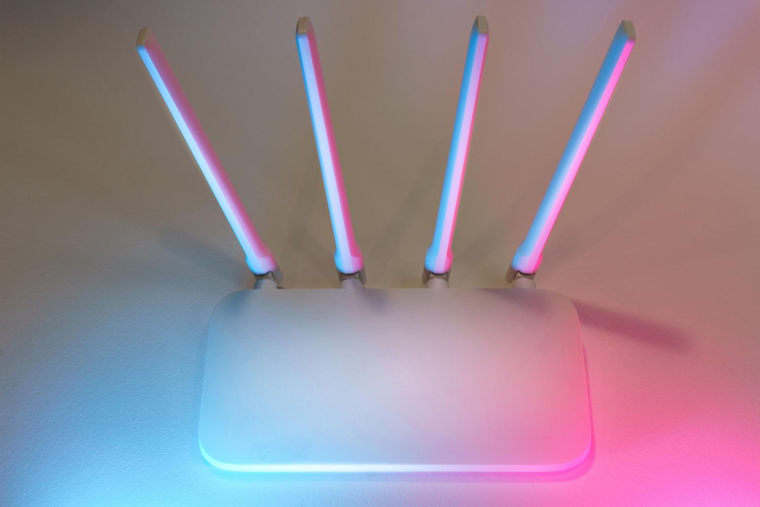 Router inalámbrico blanco moderno con cuatro antenas verticales sobre fondo blanco con luces ambientales azul y rosa