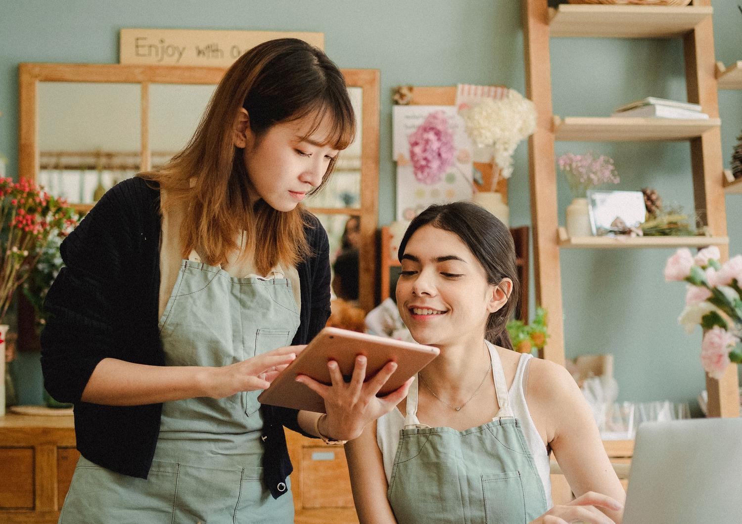 Floristas en una pequeña empresa utilizando laptops y tablets para gestionar sus pedidos, ejemplificando la digitalización de negocios tradicionales.