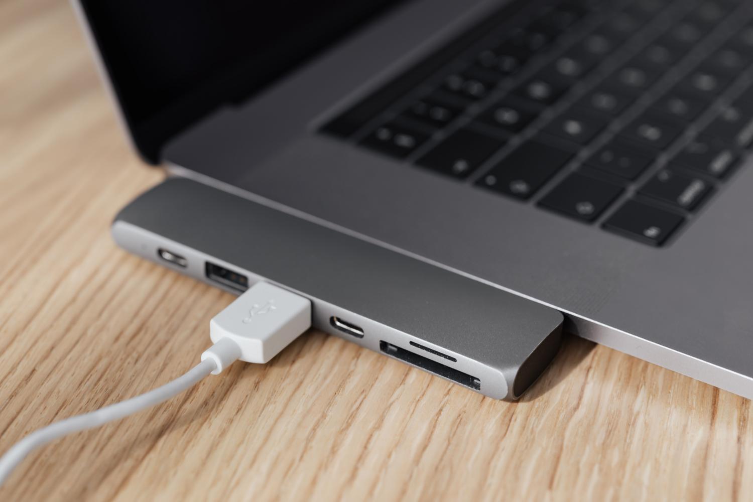 Portátil moderno con un hub multiport USB-C conectado y cables de carga. Portátil moderno con un hub multiport USB-C conectado y cables de carga.