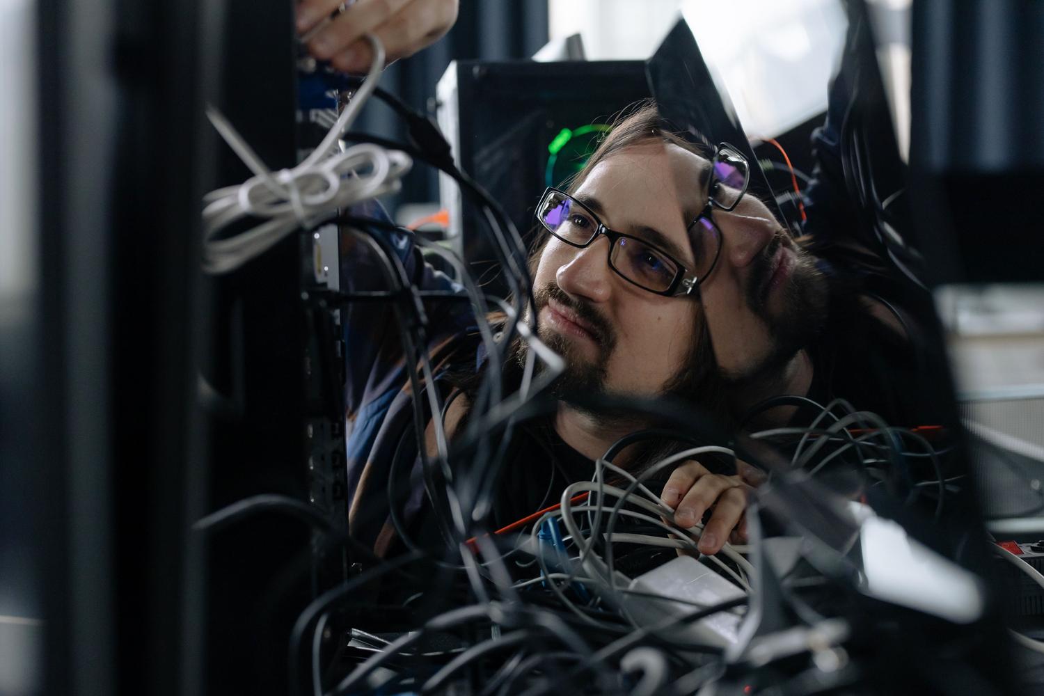 Técnico informático organizando cables detrás de un ordenador en una oficina, ilustrando el proceso de diagnóstico de hardware.