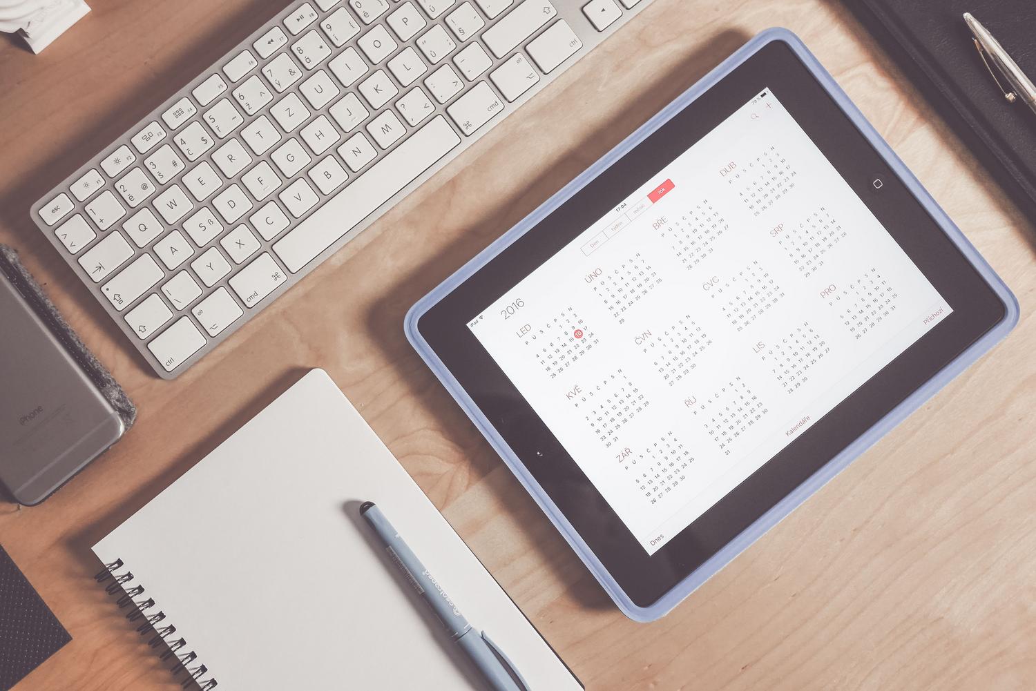 Escritorio organizado con una tablet mostrando un calendario, teclado y cuaderno, representando la digitalización de la agenda. Escritorio organizado con una tablet mostrando un calendario, teclado y cuaderno, representando la digitalización de la agenda.