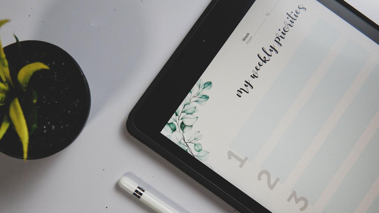 Primer plano de una tablet con un planificador de prioridades semanales y un lápiz digital sobre un escritorio blanco. Primer plano de una tablet con un planificador de prioridades semanales y un lápiz digital sobre un escritorio blanco.
