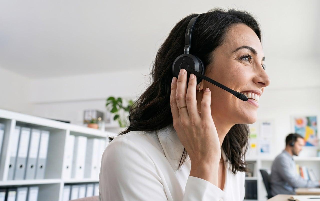 Mujer profesional de atención al cliente sonriendo con auriculares en una oficina moderna.
