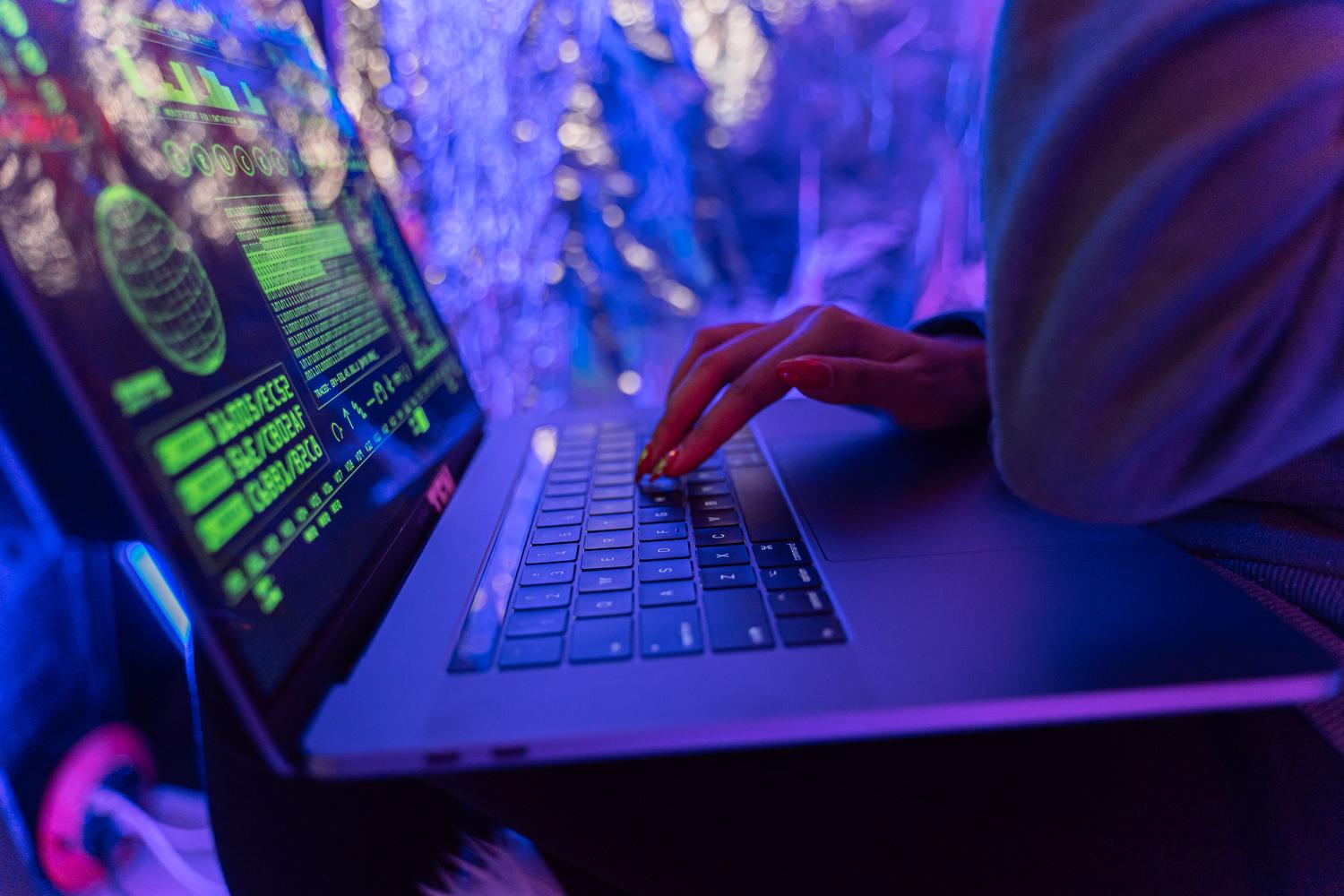 Manos escribiendo en un teclado de portátil con gráficos de ciberseguridad iluminados en tonos púrpuras, enfatizando el entorno técnico de la seguridad informática. Manos escribiendo en un teclado de portátil con gráficos de ciberseguridad iluminados en tonos púrpuras, enfatizando el entorno técnico de la seguridad informática.