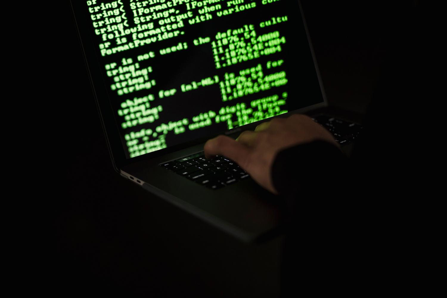 Una persona encapuchada escribiendo en un ordenador portátil en la oscuridad, representando la amenaza del malware y los ciberataques. Una persona encapuchada escribiendo en un ordenador portátil en la oscuridad, representando la amenaza del malware y los ciberataques.