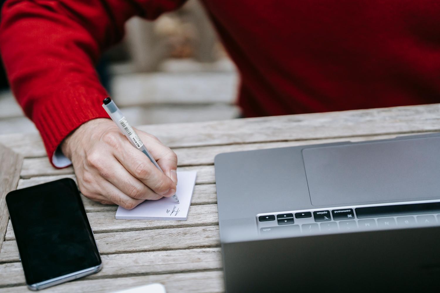 Persona tomando notas junto a un portátil y móvil en un entorno exterior, ilustrando la productividad móvil y el enfoque offline-first.