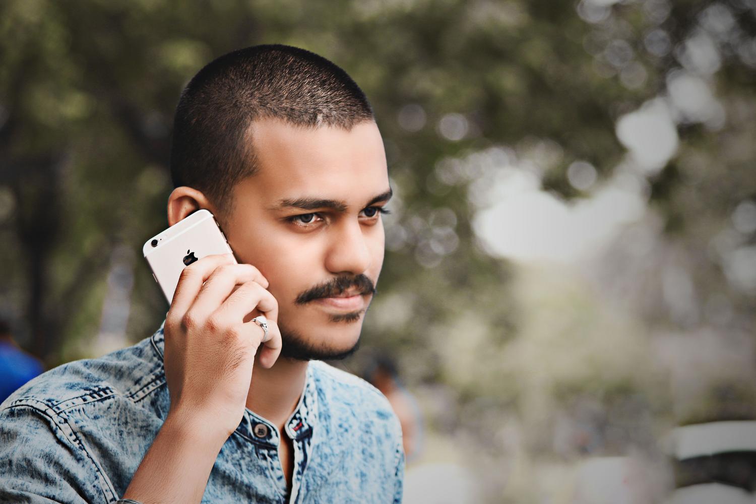 Primer plano de un hombre joven utilizando un smartphone con expresión concentrada al aire libre.