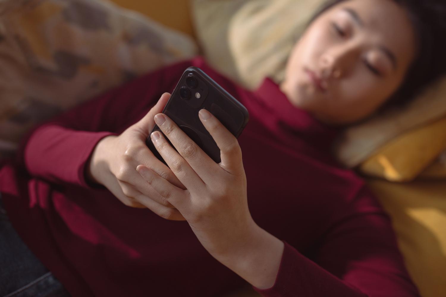 Mujer joven tumbada cómodamente en casa usando su smartphone en un ambiente de relajación.