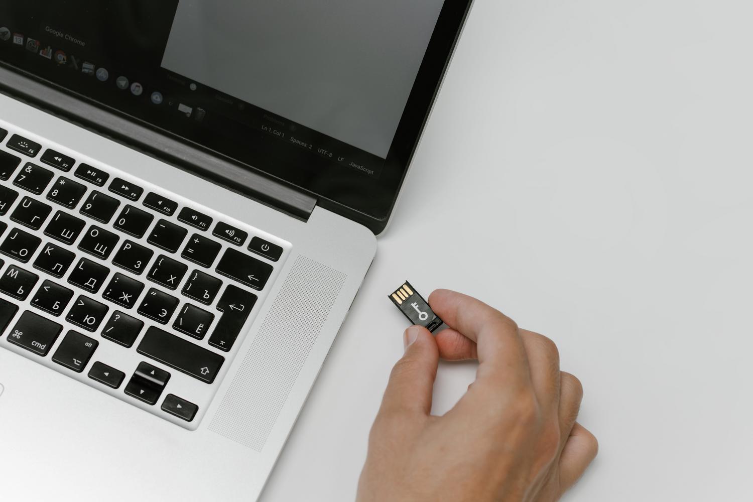 Mano insertando una memoria USB en un ordenador portátil, ilustrando la creación de medios de instalación ISO.