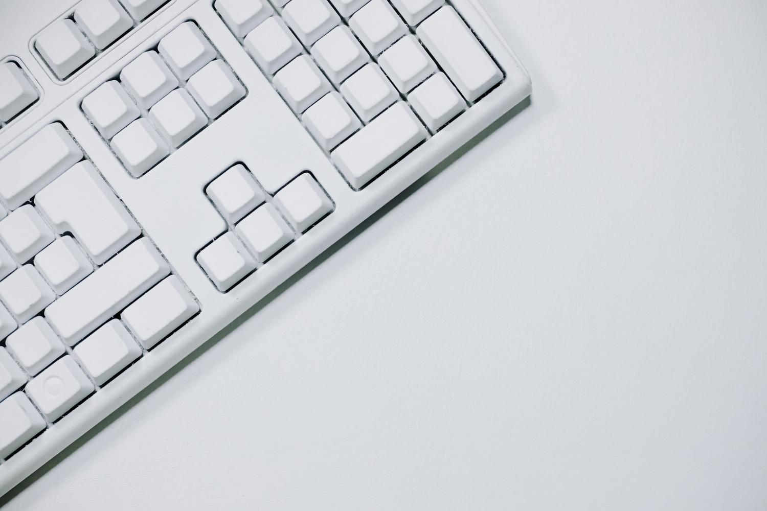 Minimalistická bílá mechanická klávesnice na bílém pozadí, ideální pro profesionální technologickou hlavičku