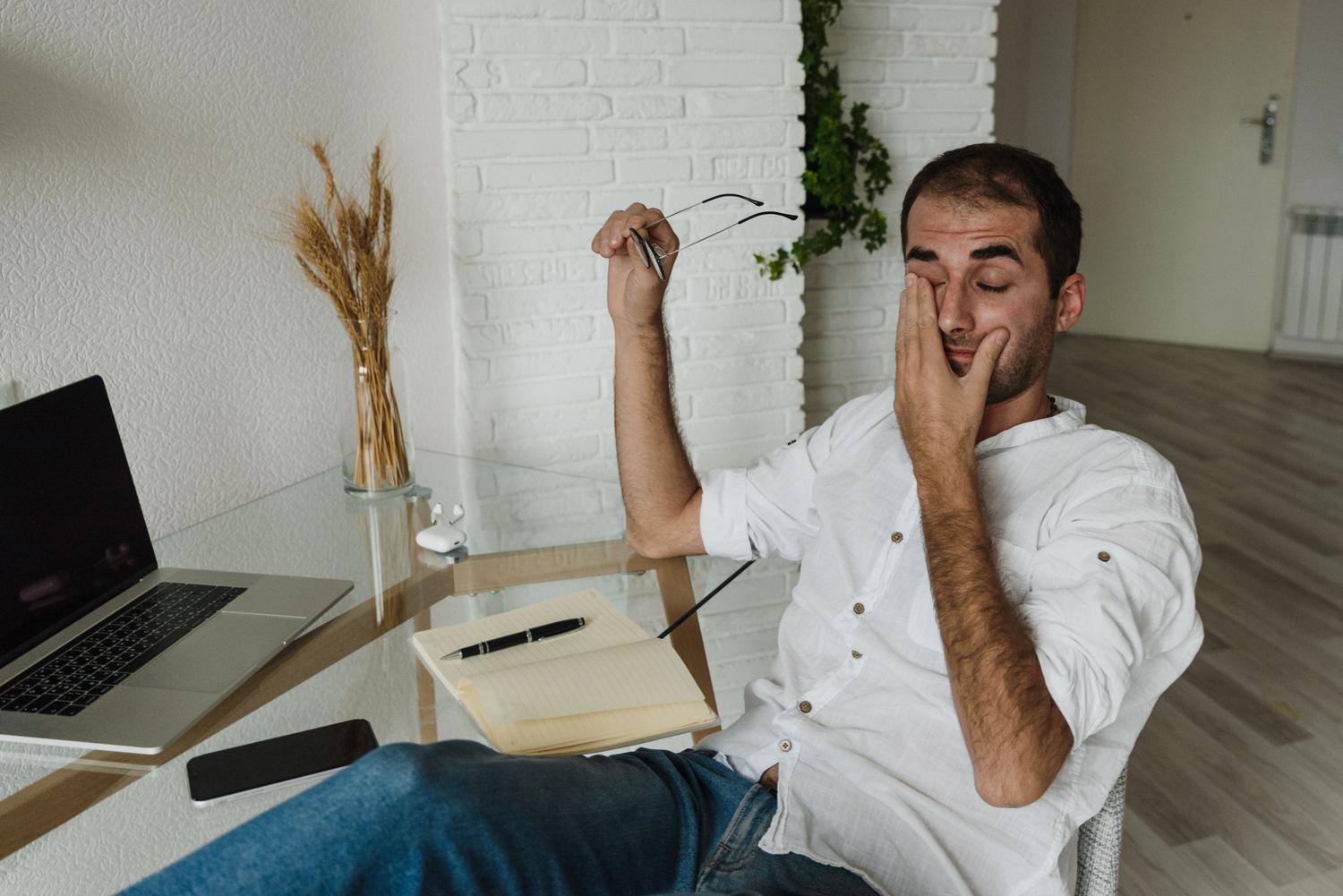 Hombre cansado frotándose los ojos frente a un escritorio, ejemplificando la fatiga visual y el síndrome de visión informática.