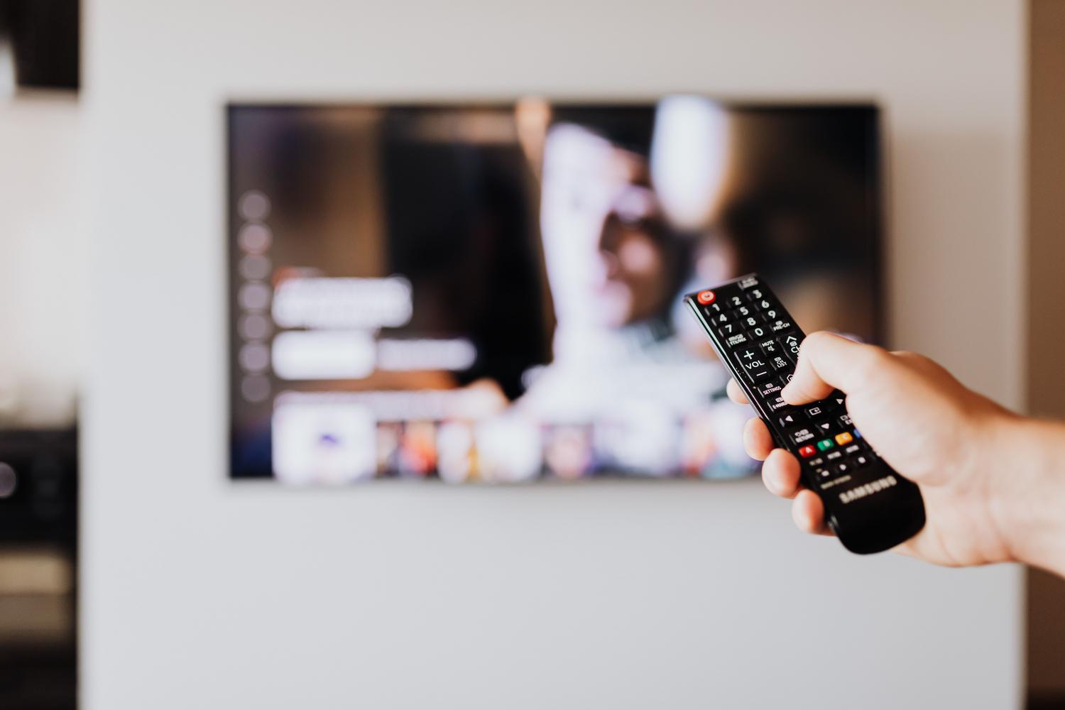 Primer plano de una mano utilizando el mando a distancia de una Smart TV para navegar por los ajustes.