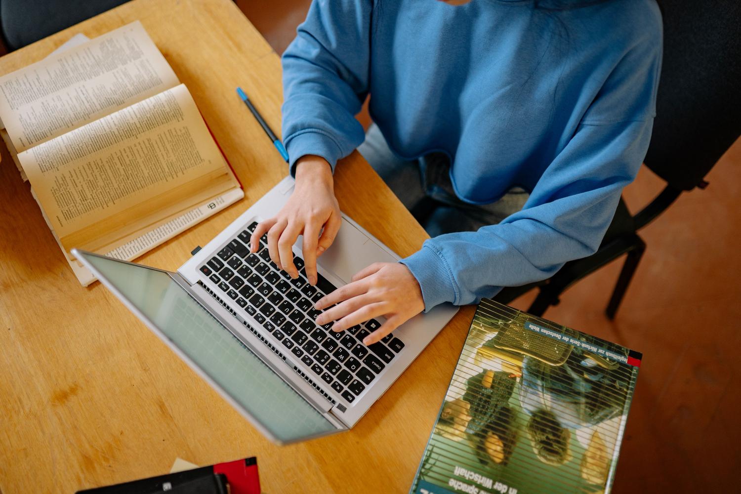 Egy laptopot használó személy könyvekkel körülvéve, egy digitális gyűjtemény rendszerezését illusztrálva.