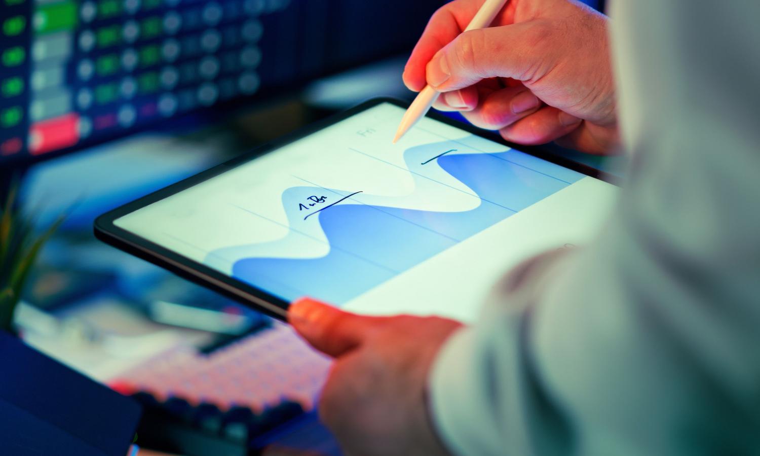 Profesional analizando gráficos de datos en una tablet con un lápiz óptico en un entorno de oficina moderna.