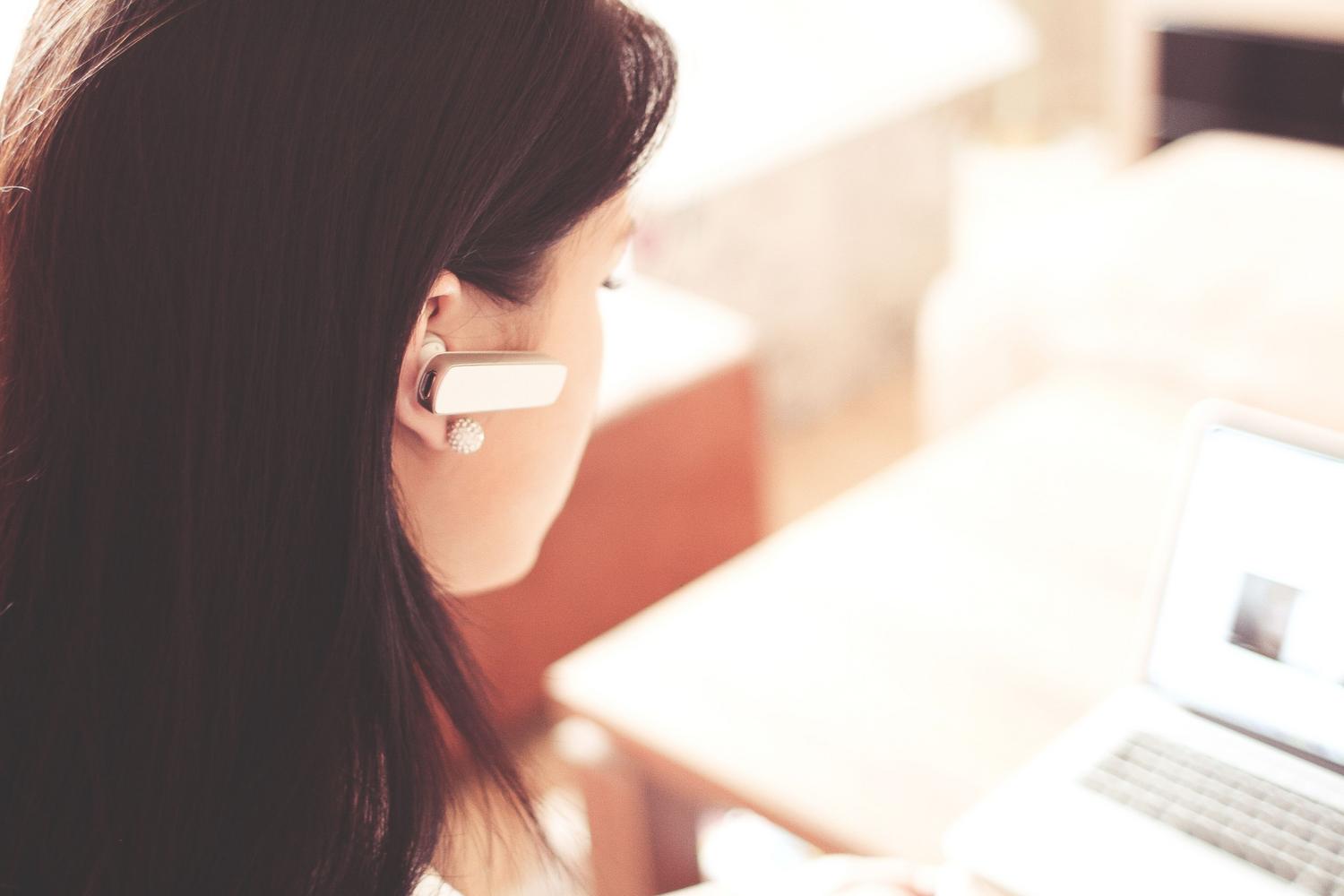 Mujer profesional en una oficina utilizando un auricular Bluetooth conectado a su ordenador portátil.