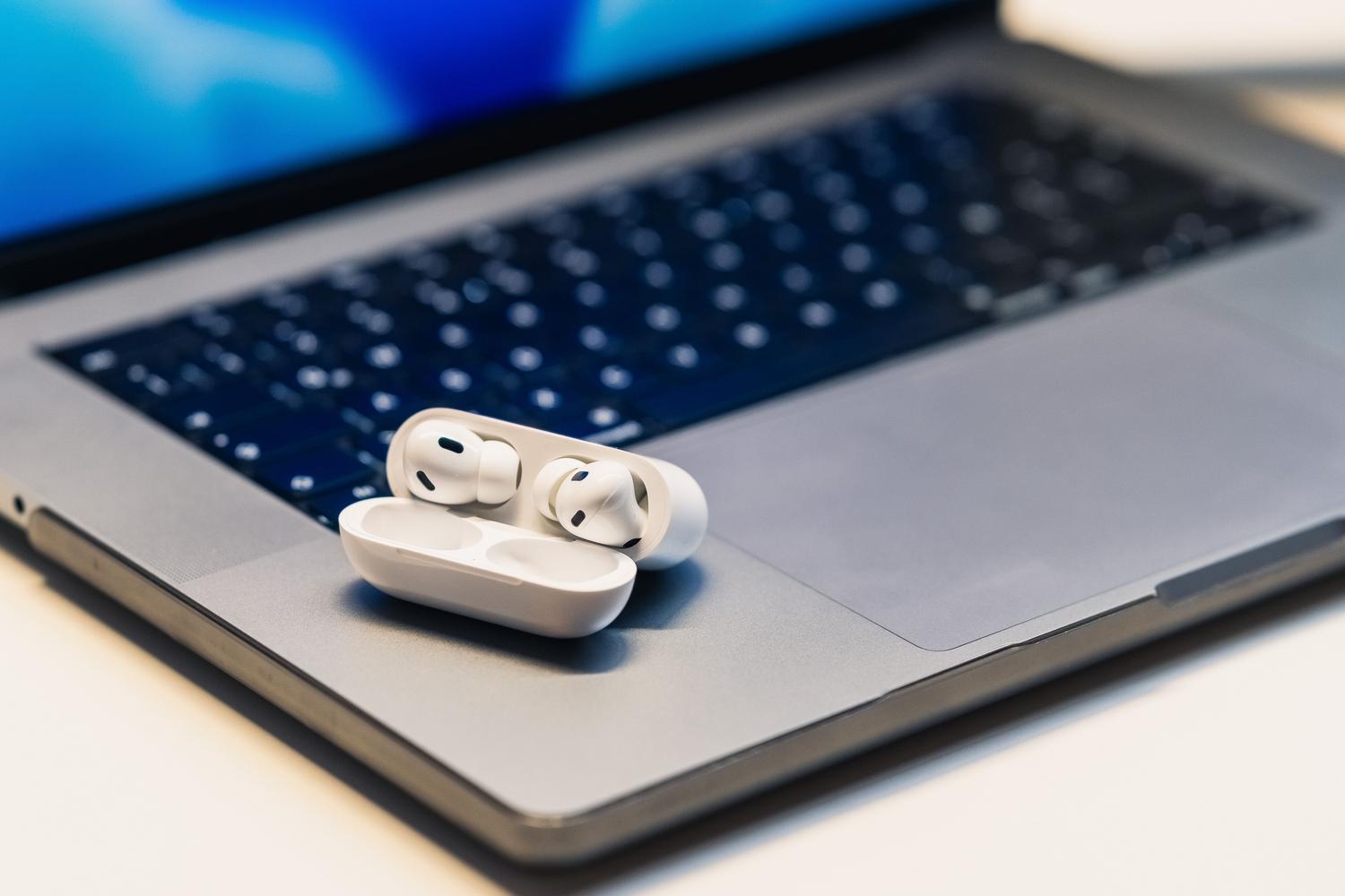 Primer plano de auriculares inalámbricos sobre un ordenador portátil, representando problemas de audio Bluetooth.