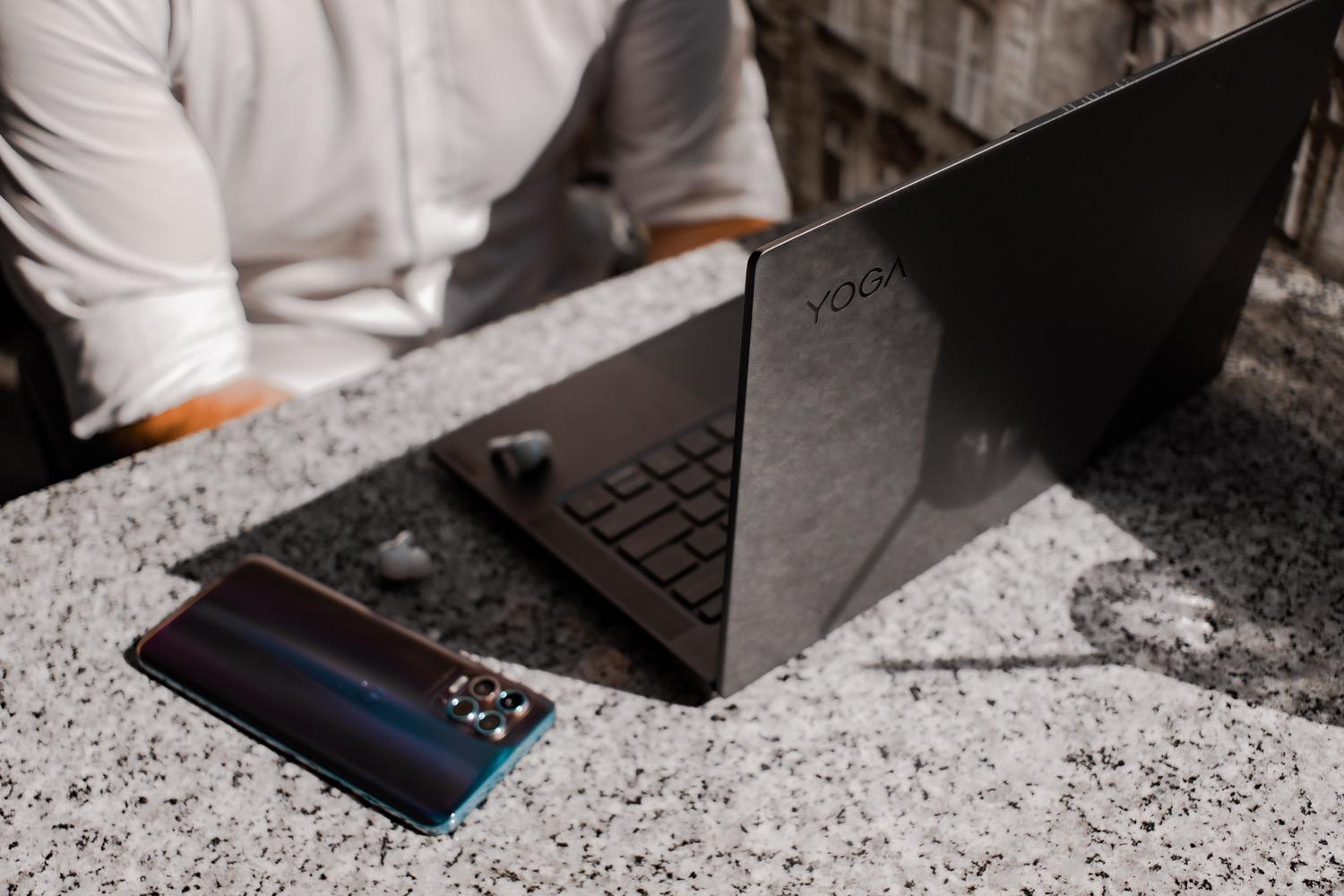 Ecosistema de dispositivos conectados con portátil y auriculares Bluetooth sobre una superficie de granito.