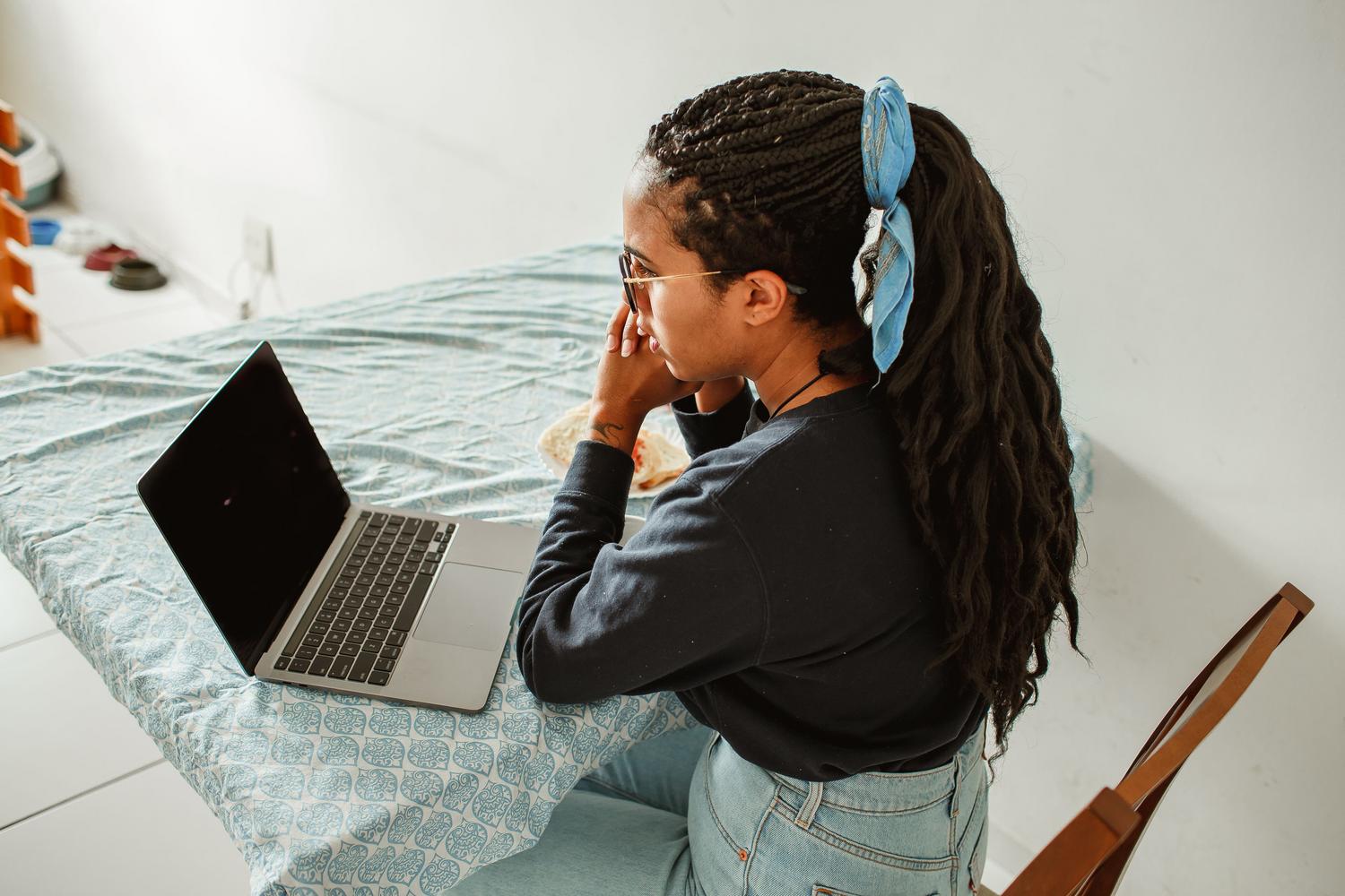 Mujer joven enfocada estudiando con su portátil en una mesa en casa, ilustrando la creación de rutinas de estudio semanales eficientes