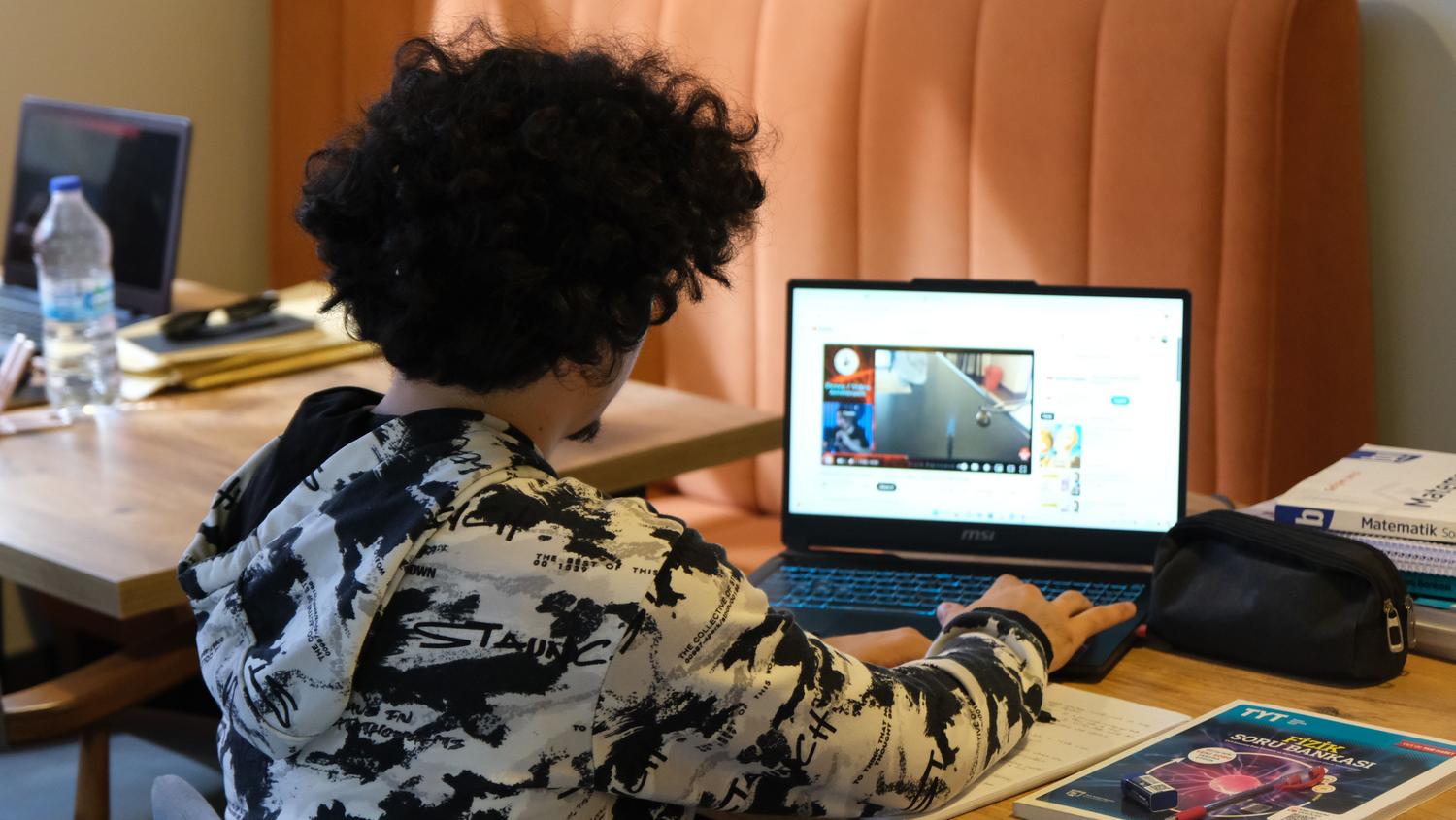 Joven estudiando en casa integrando materiales físicos como libros con el uso de un ordenador portátil para el aprendizaje digital