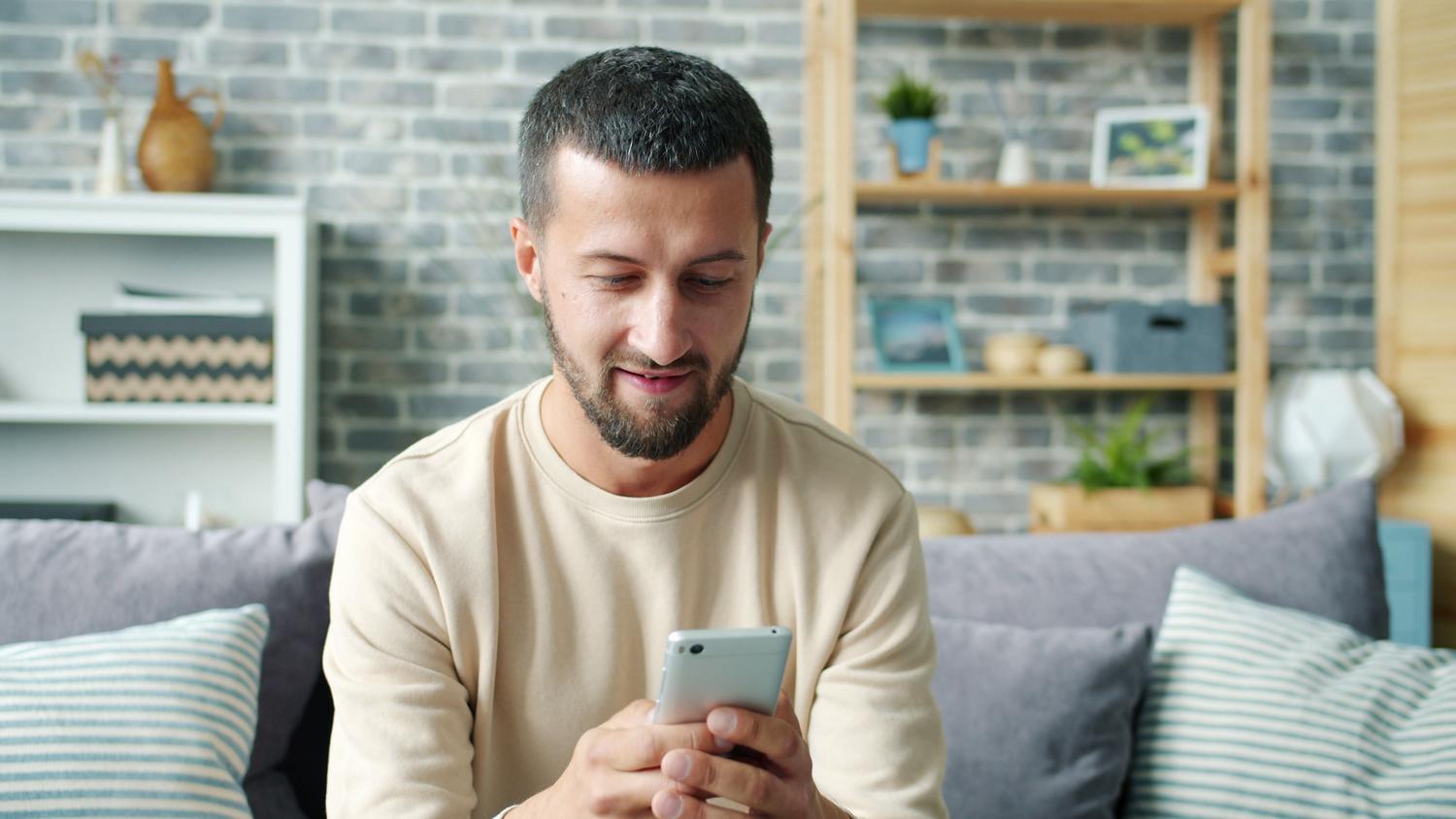 Persona utilizando un smartphone relajadamente en el sofá de un salón moderno.