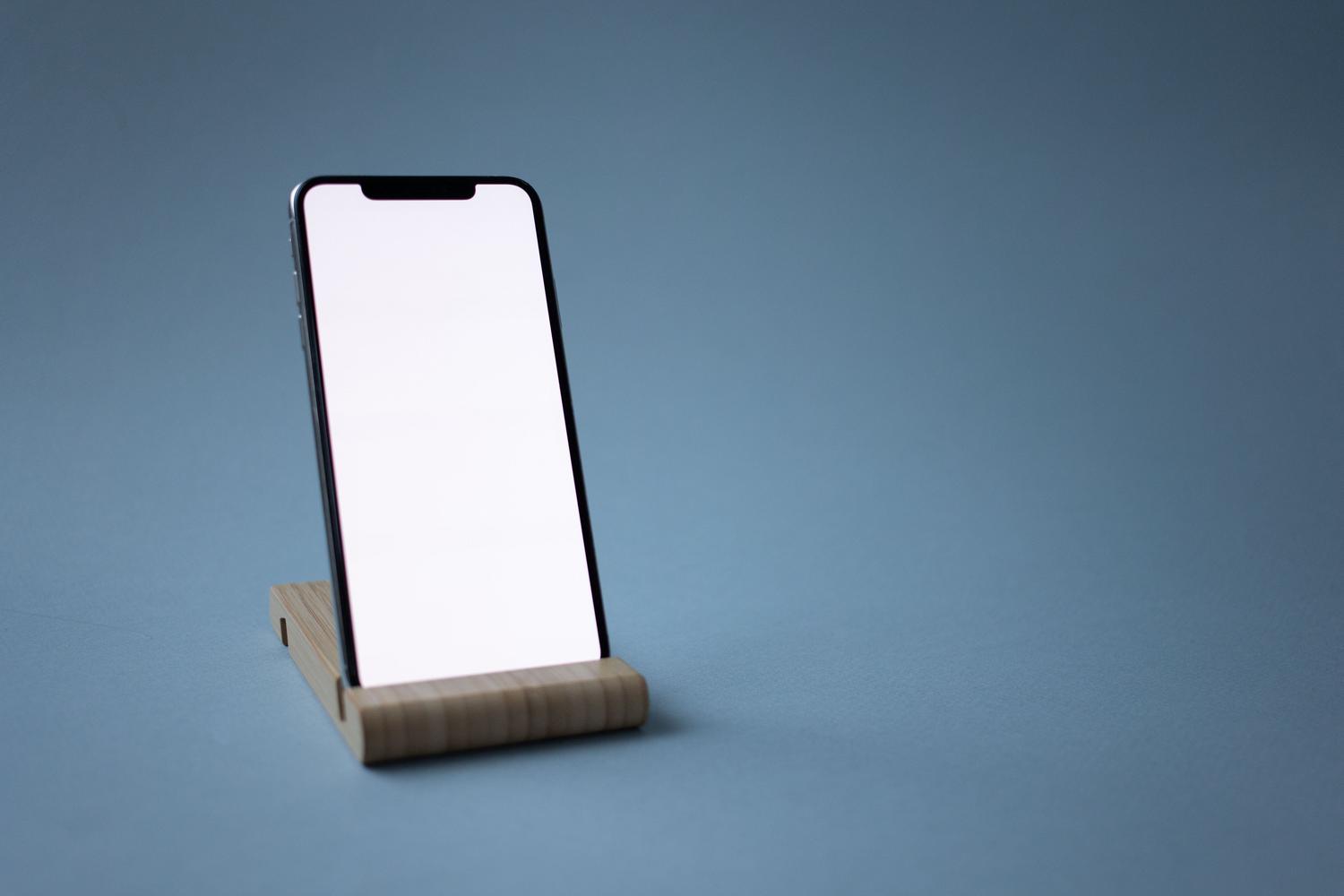 Smartphone colocado en un soporte de madera minimalista, ilustrando la importancia de la ergonomía y el uso de soportes para el móvil.