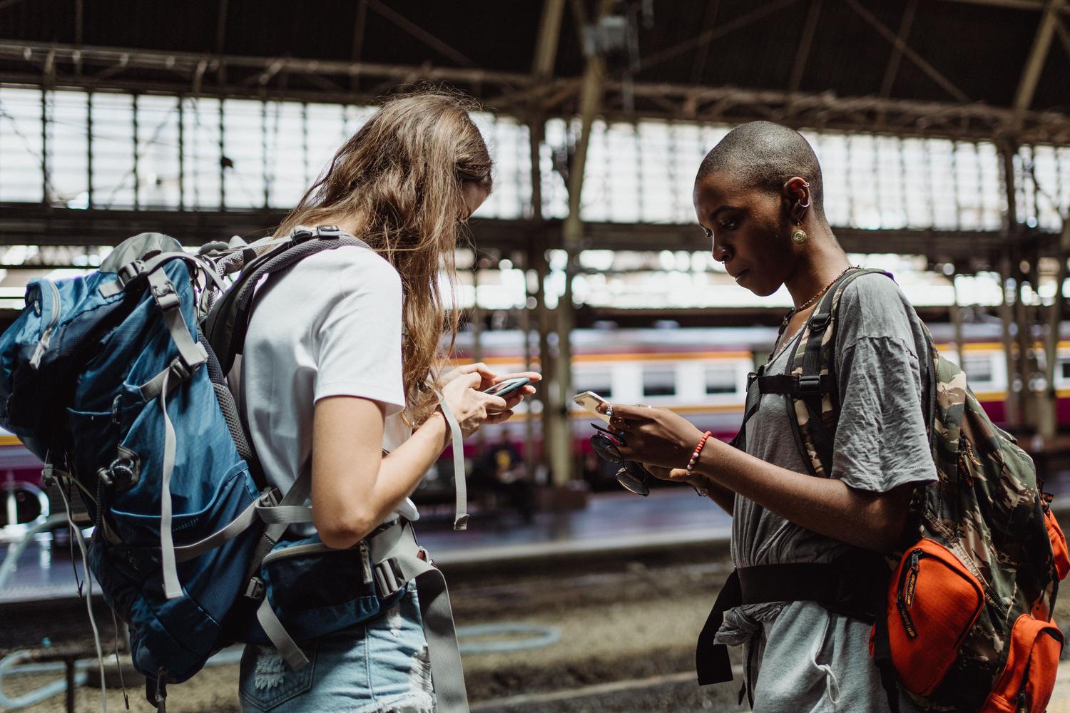 Dos mochileros consultando su teléfono móvil mientras esperan en una estación de tren