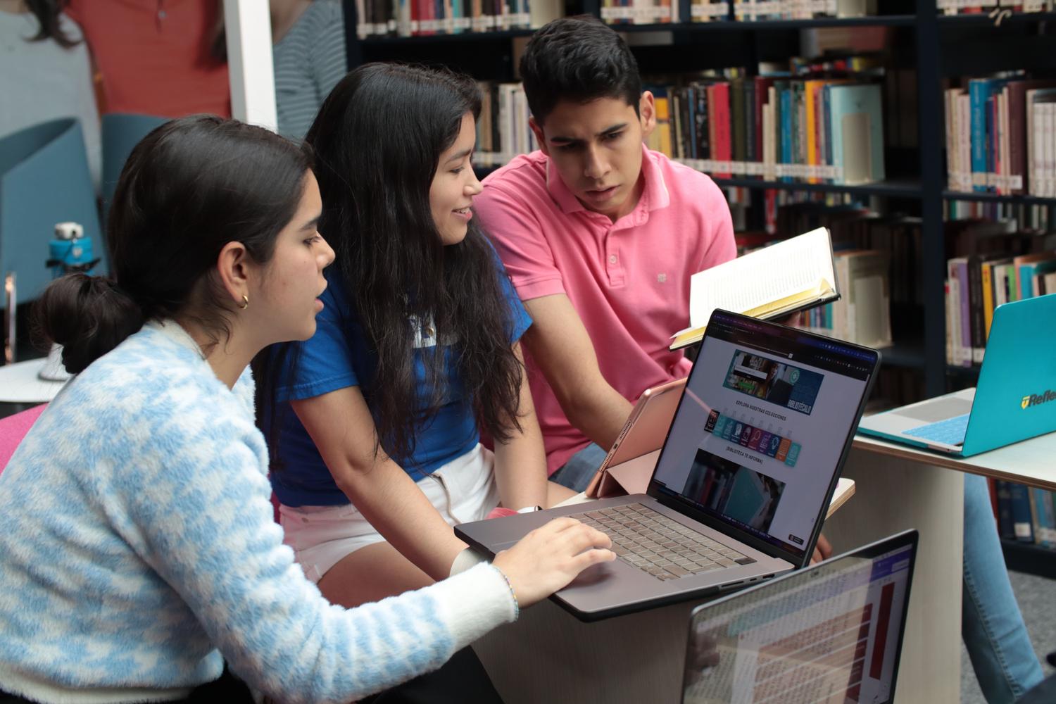 Grupo de estudiantes universitarios estudiando y colaborando en una biblioteca con laptops y libros.