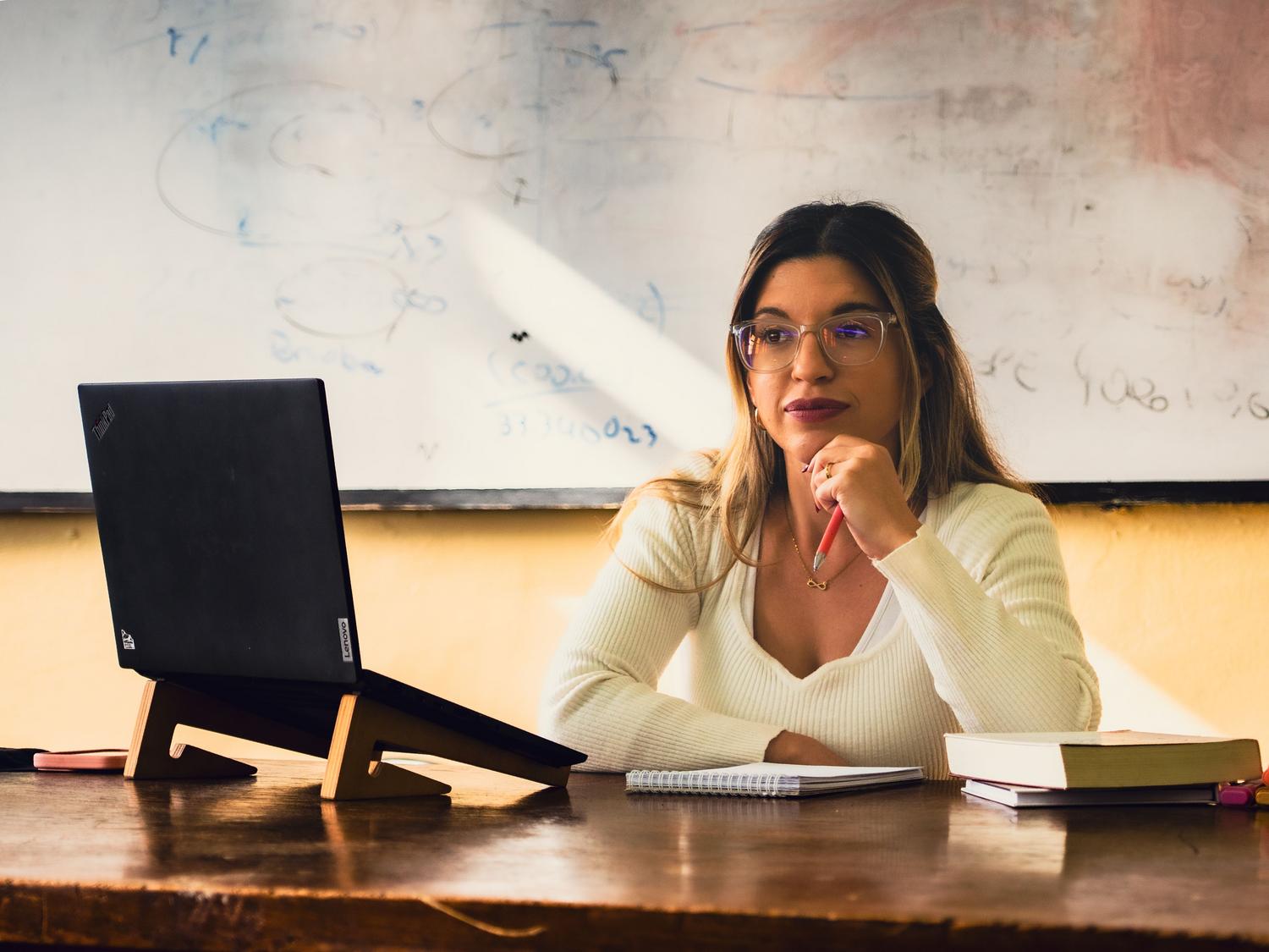 Mujer joven estudiando concentrada en su escritorio con un ordenador portátil y apuntes.